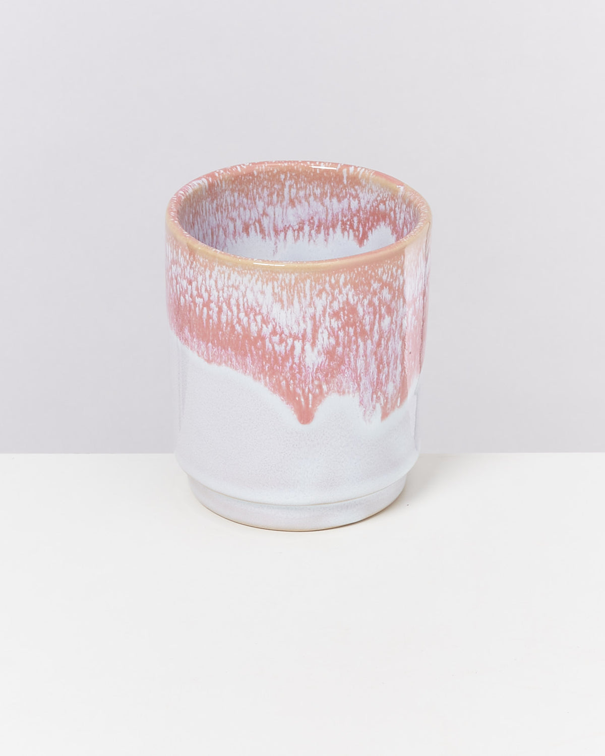 Keramiktasse mit rosa-weißem Muster auf weißem Hintergrund.