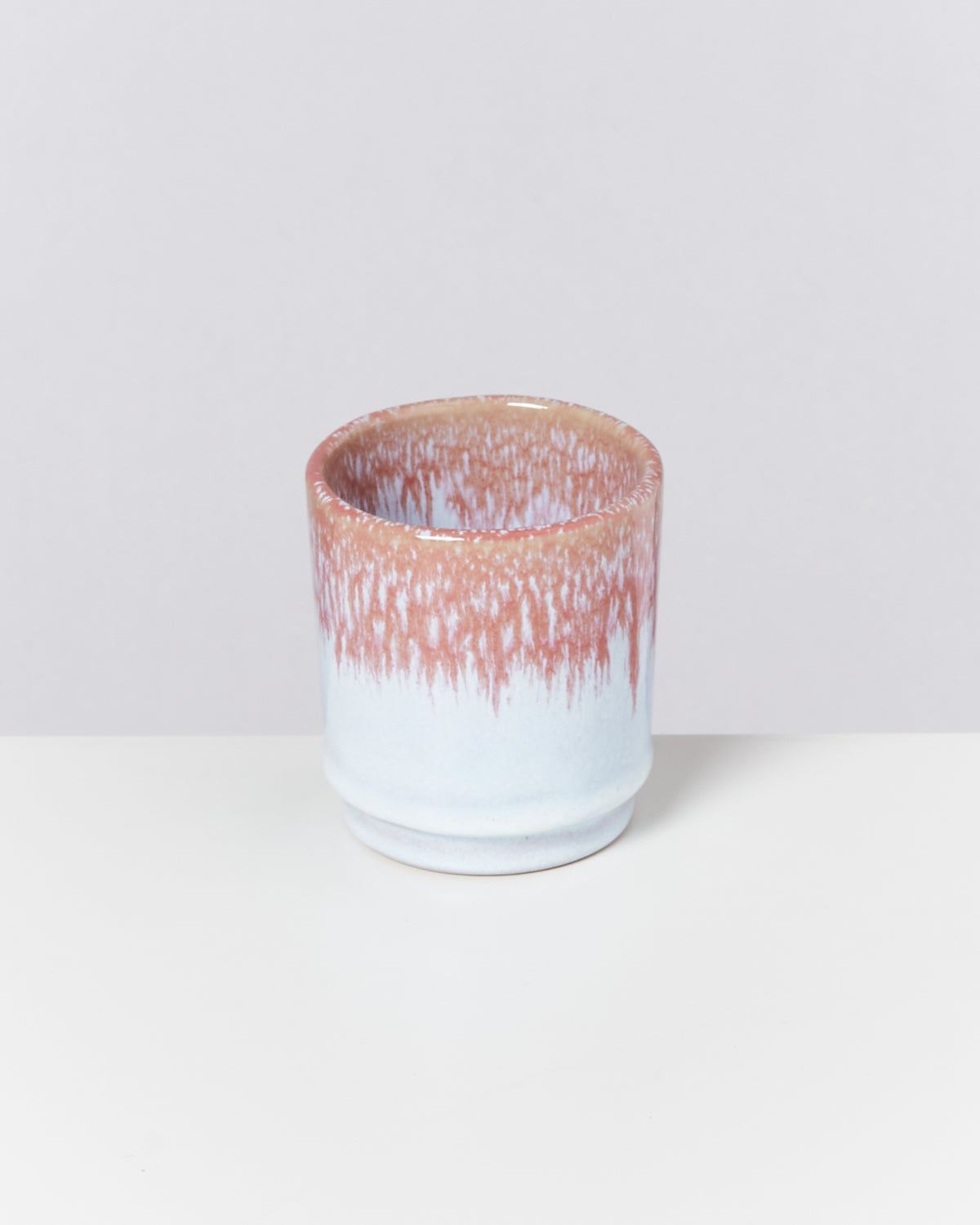 Keramikbecher mit weiß-roter Glasur auf einem weißen Hintergrund.