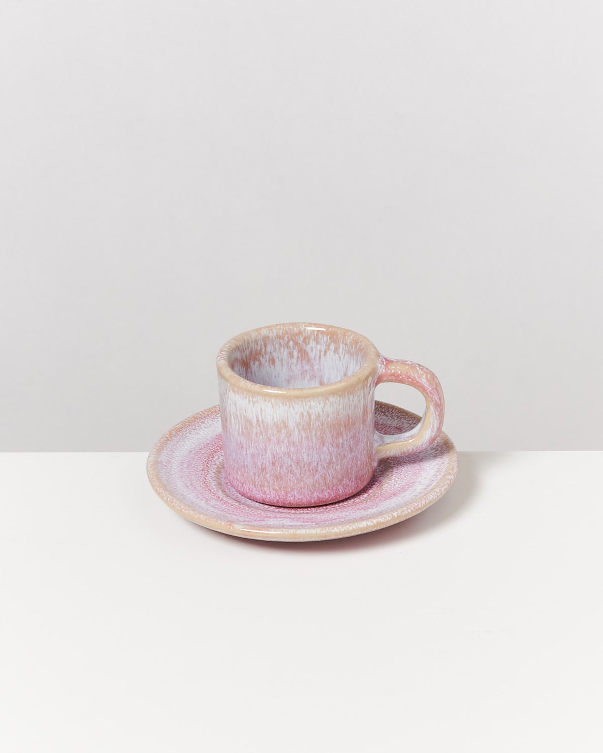 Eine rosa-weiße Tasse mit Untertasse steht auf einem weißen Tisch vor einem hellen Hintergrund.