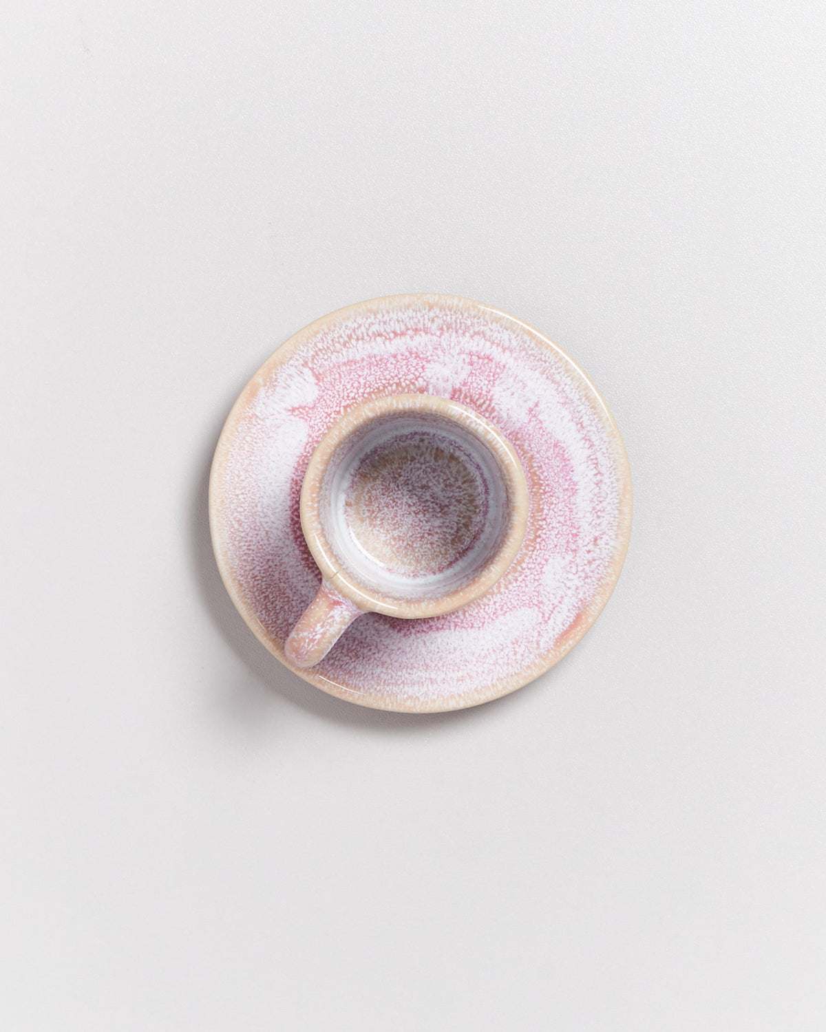 Keramiktasse mit Untertasse in Rosa- und Beigetönen, von oben fotografiert, auf hellem Hintergrund.