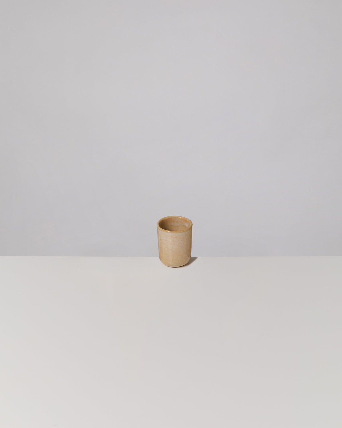 Brauner Becher auf weißem Tisch vor einem grauen Hintergrund.