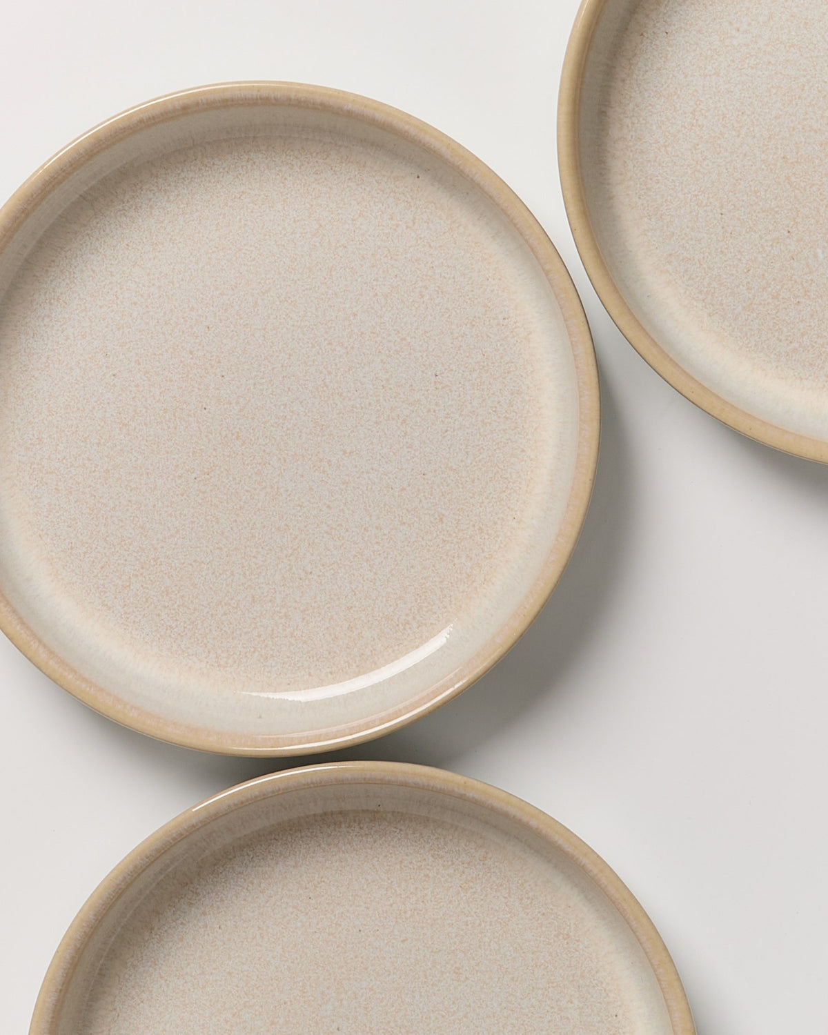 Drei beige Keramikteller mit leicht gesprenkelter Oberfläche auf weißem Hintergrund.