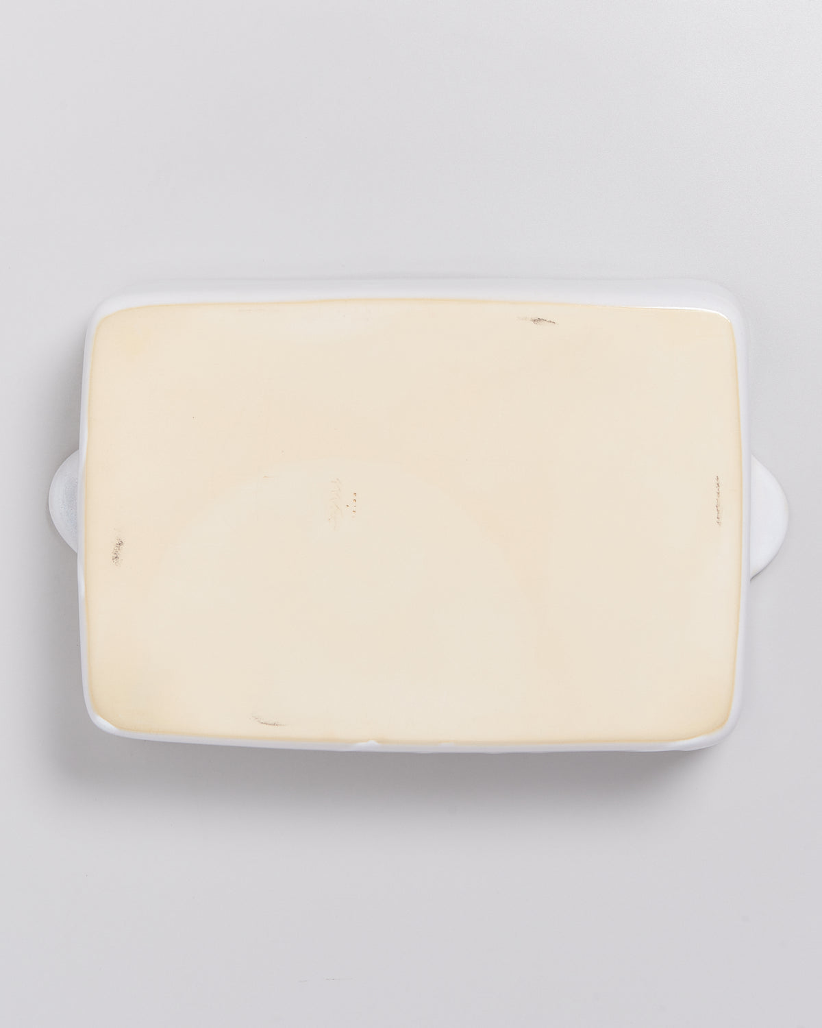 Rechteckige beige Keramikplatte mit einem leichten Rand auf einem grauen Hintergrund.