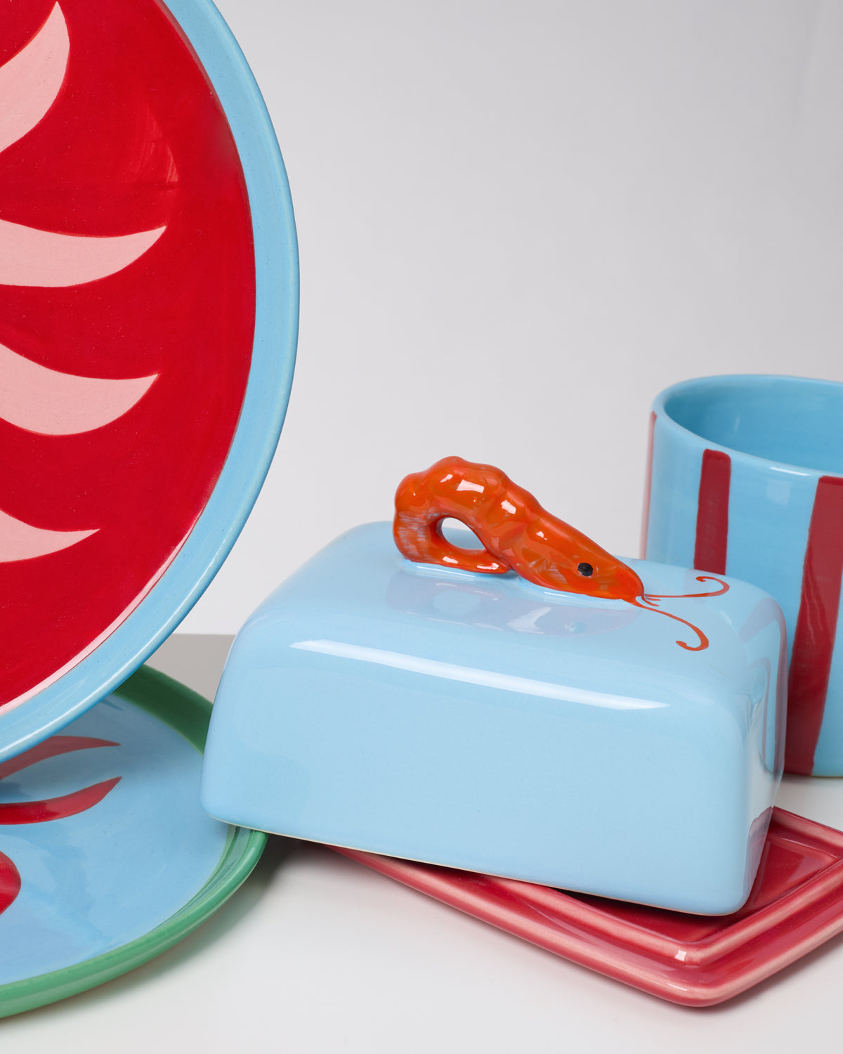 Buntes Keramikgeschirr mit roten Motiven und einer Garnelenfigur auf einer Butterdose.