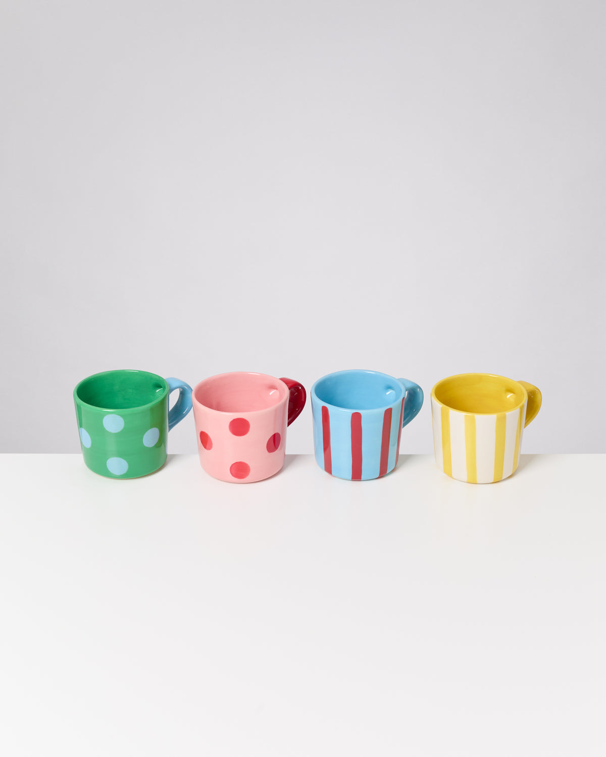 Vier bunte Tassen mit unterschiedlichen Mustern stehen in einer Reihe auf einem weißen Tisch.