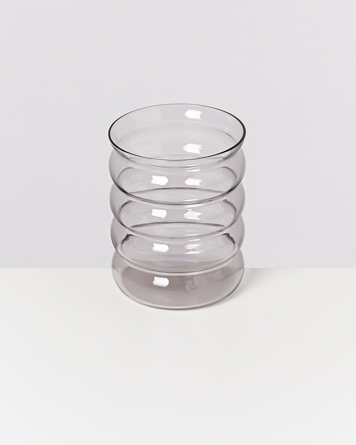 Klares Glas mit geschwungenen Faltlinien, auf einem weißen Hintergrund stehend.