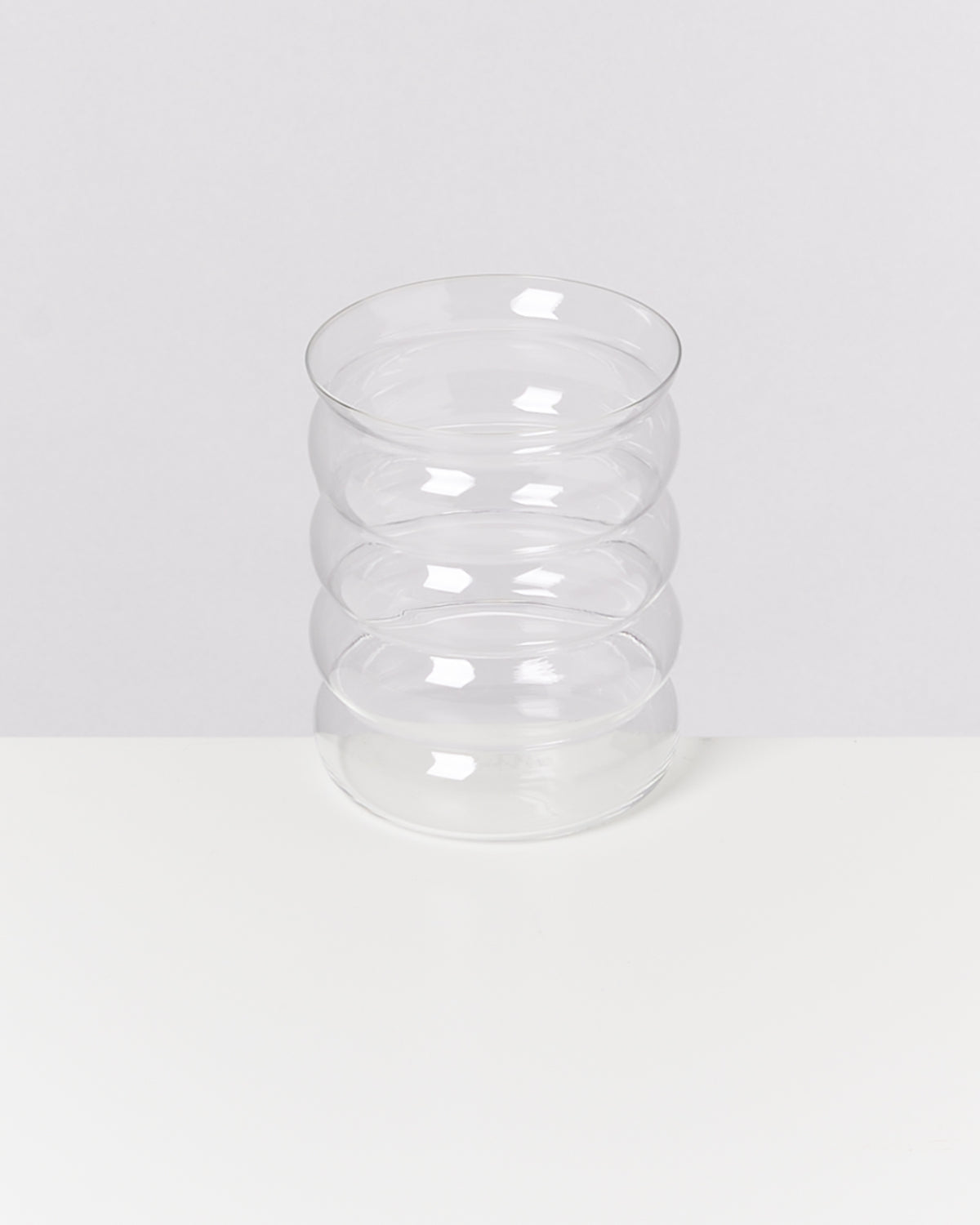 Ein transparentes Glas mit wellenförmigen Rillen steht auf einer weißen Oberfläche.