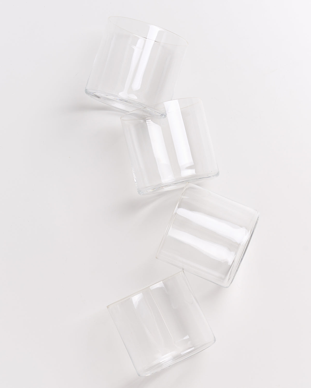 Vier leere, transparente Gläser liegen diagonal auf einer weißen Oberfläche.