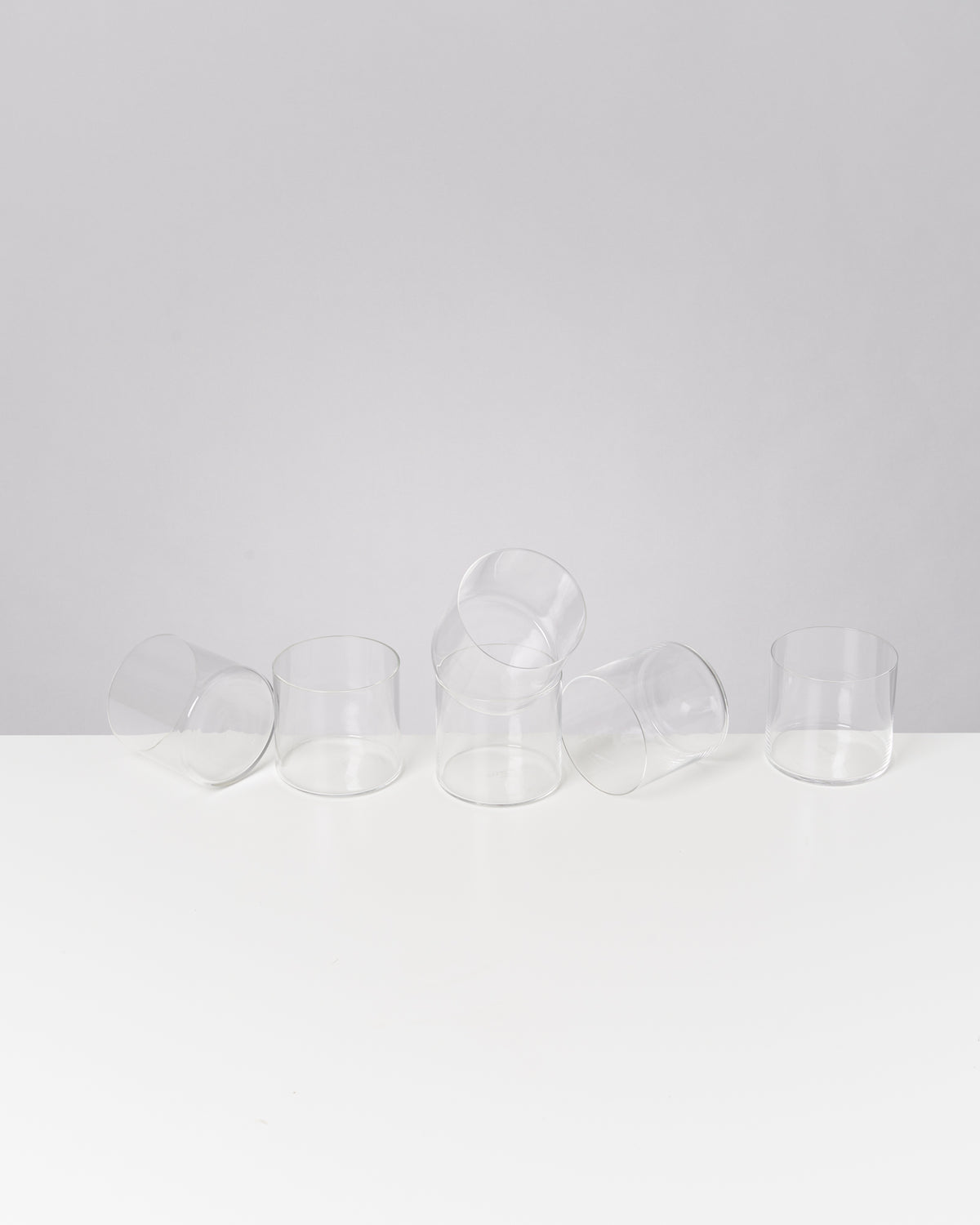 Sechs leere Glasbecher auf einem weißen Tisch, einige stehen aufrecht, andere liegen auf der Seite.