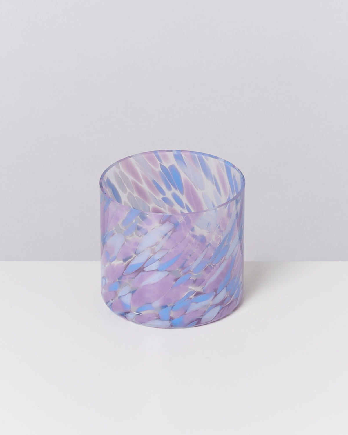 Ein Glasbecher mit lila und blauen Marmorierungsmustern auf einem weißen Hintergrund.