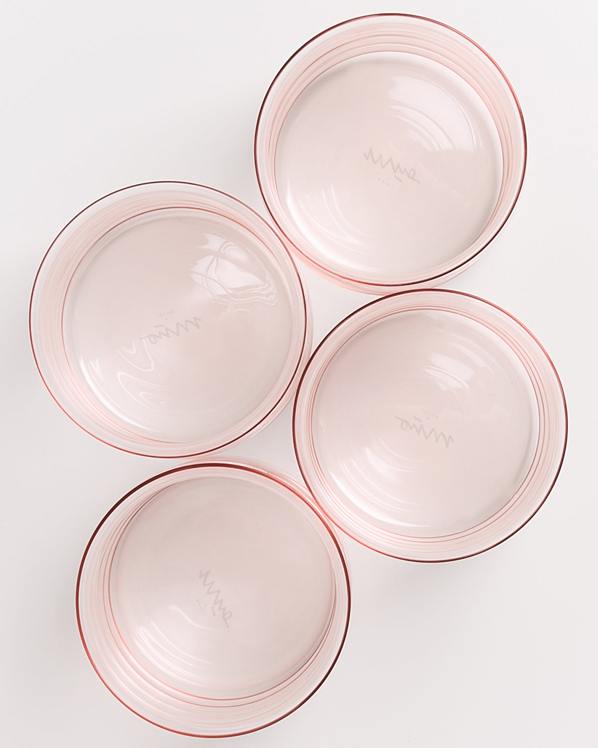 Vier rosa Glasschüsseln mit feinen Streifen, symmetrisch auf einer weißen Oberfläche angeordnet.