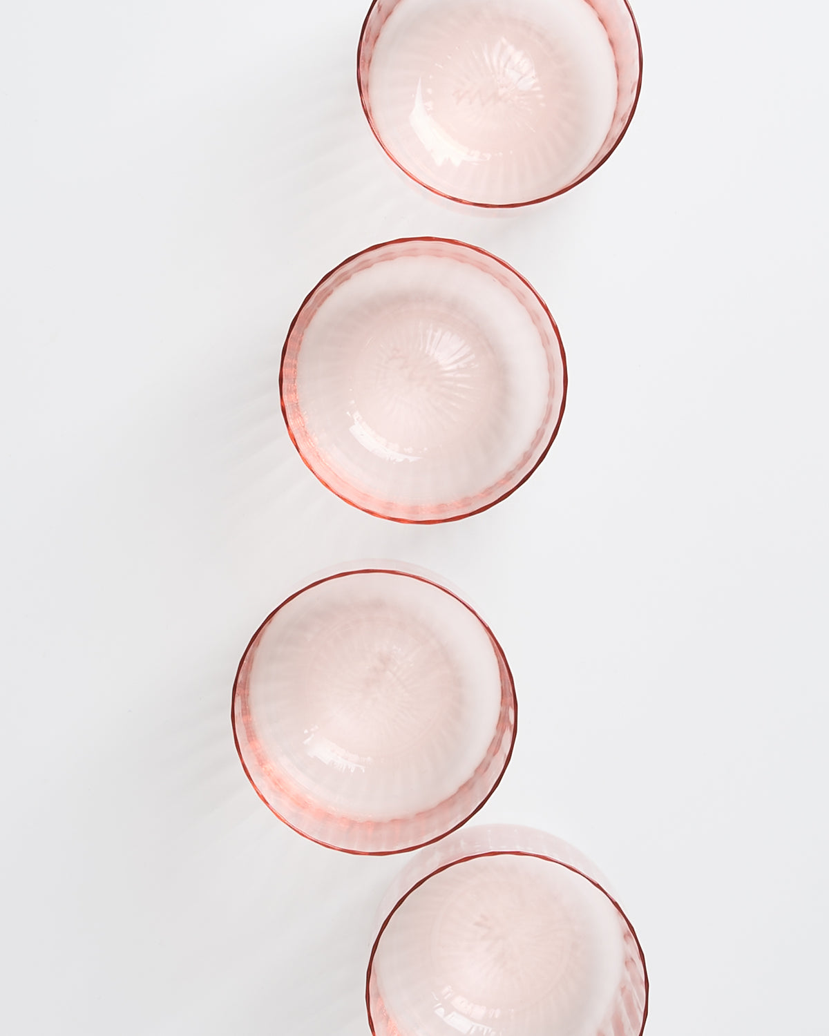 Vier rosafarbene Glasschalen mit rotem Rand sind in einer vertikalen Linie auf weißem Hintergrund angeordnet.