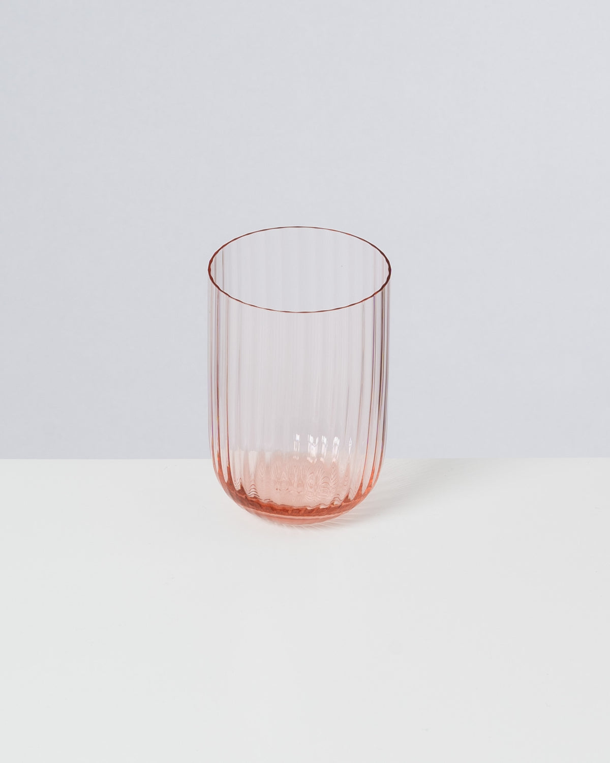 Ein geriffeltes, rosafarbenes Glas auf einer weißen Fläche vor einem grauen Hintergrund.