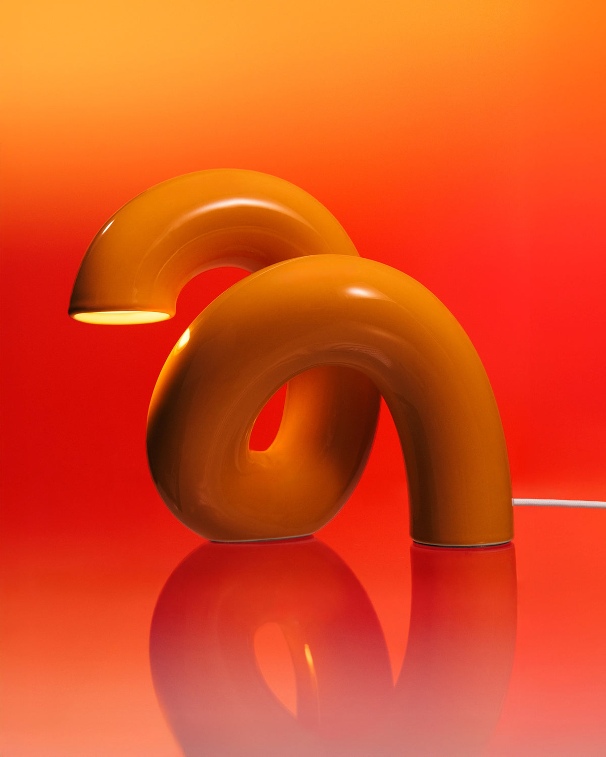 Gelbe, gebogene Tischlampe auf orangerotem Hintergrund, reflektiert auf einer glänzenden Oberfläche.
