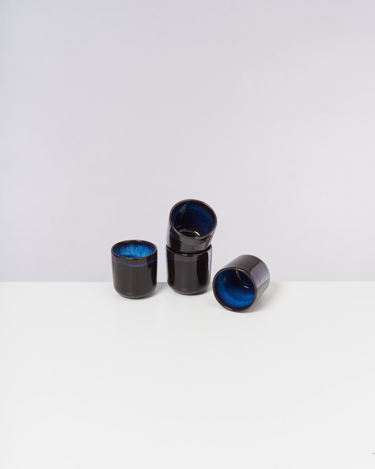 Vier schwarz-blaue Keramikbecher stehen auf einem weißen Hintergrund.