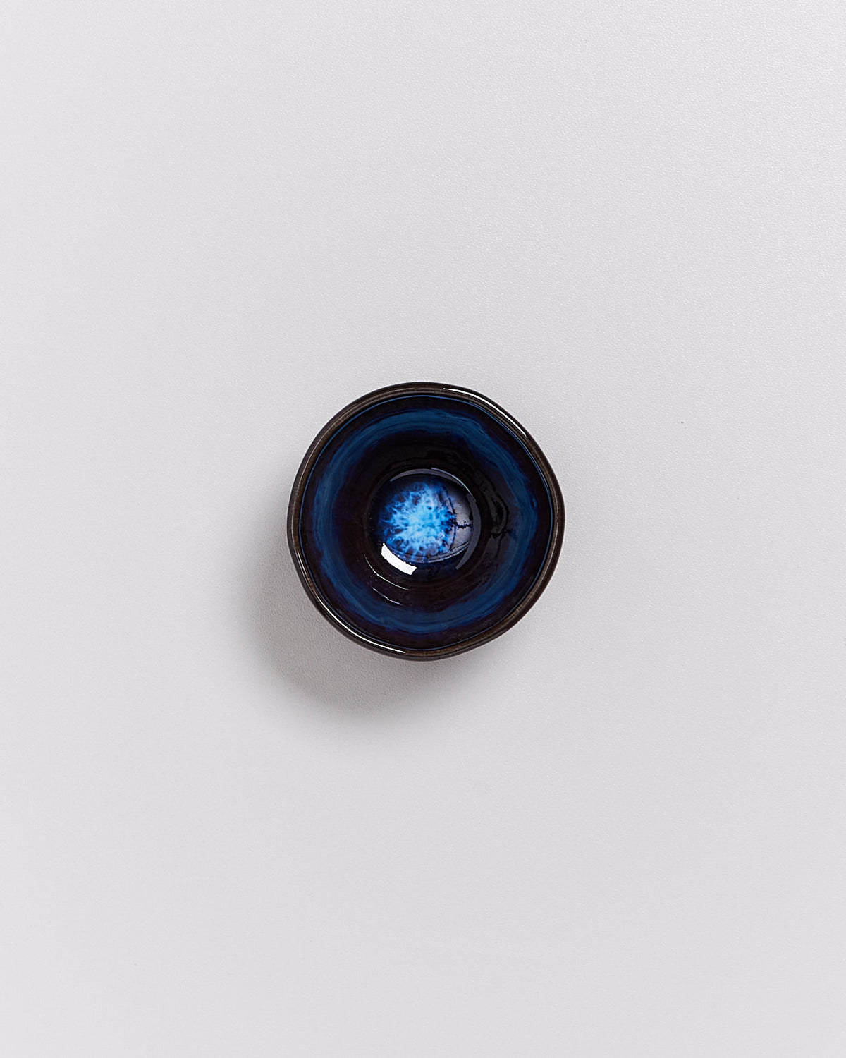 Kleine, runde, schwarze Schale mit blauer, blütenartiger Musterung in der Mitte, auf einer weißen Oberfläche.