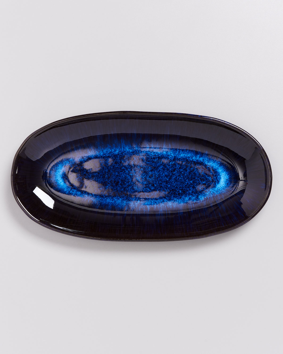 Ovaler Teller mit glänzendem, blauen und schwarzen Farbverlauf auf weißem Hintergrund.