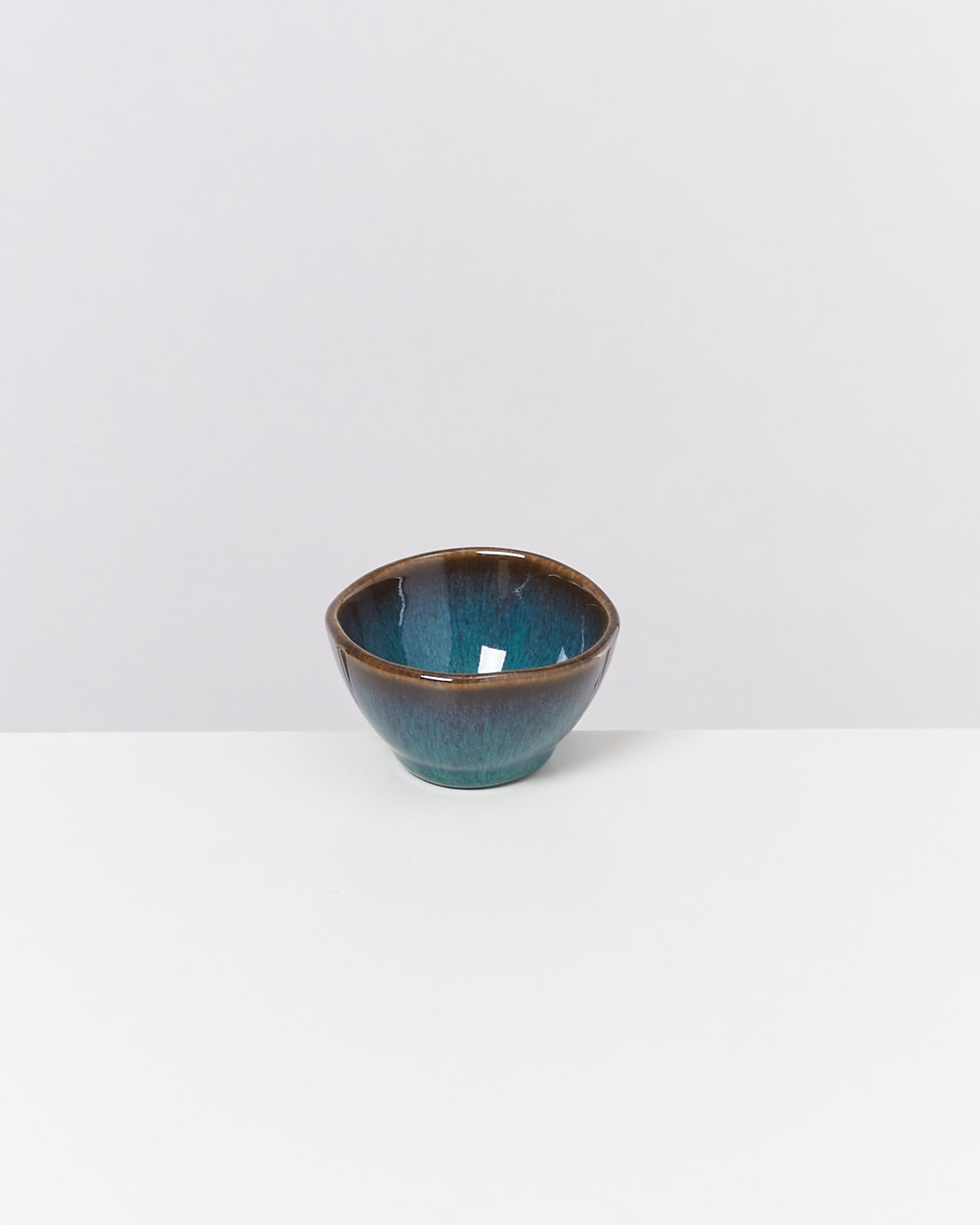 Kleine, grün-blaue Keramikschale mit braunem Rand auf weißem Hintergrund.