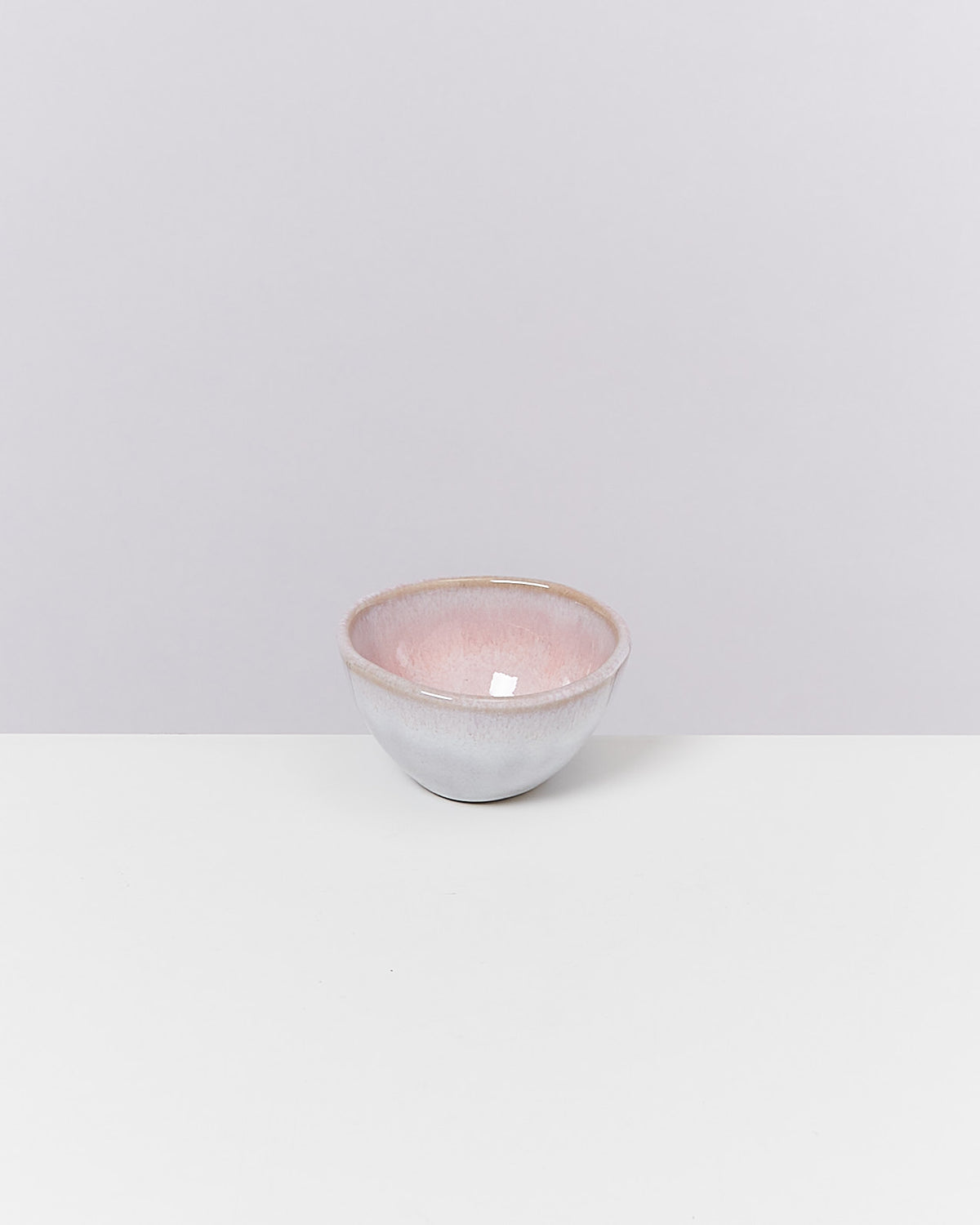 Eine kleine, pastellfarbene Keramikschale mit rosa und weißen Nuancen steht auf einem weißen Untergrund.