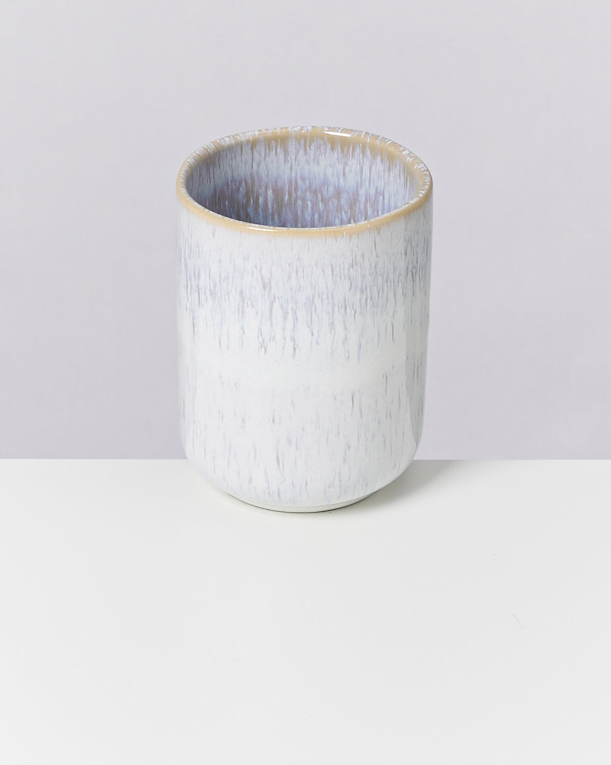 Becher aus Keramik mit blaugrauer Textur auf weißer Oberfläche.