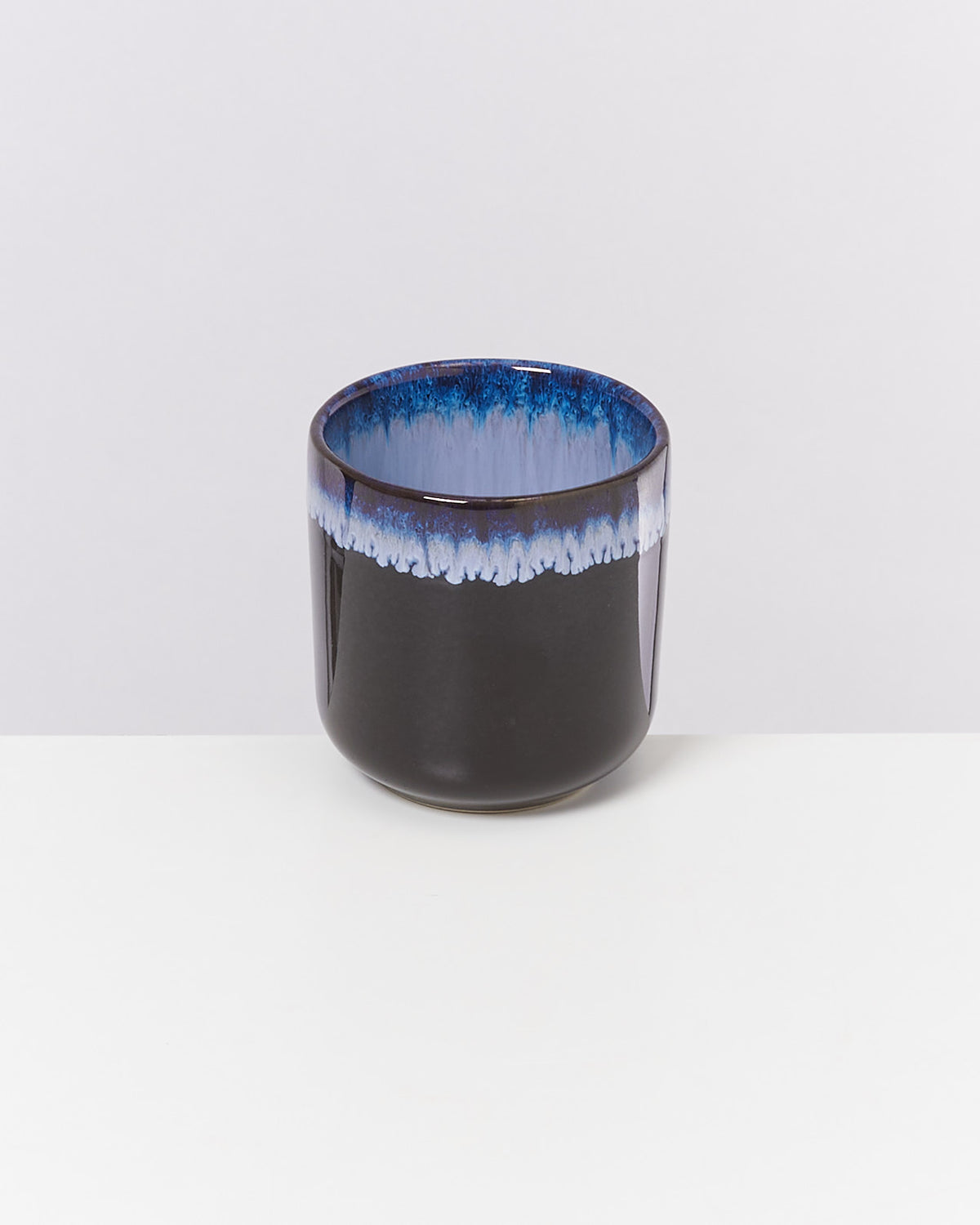 Schwarze Keramiktasse mit blau-weißem Rand auf weißem Hintergrund.