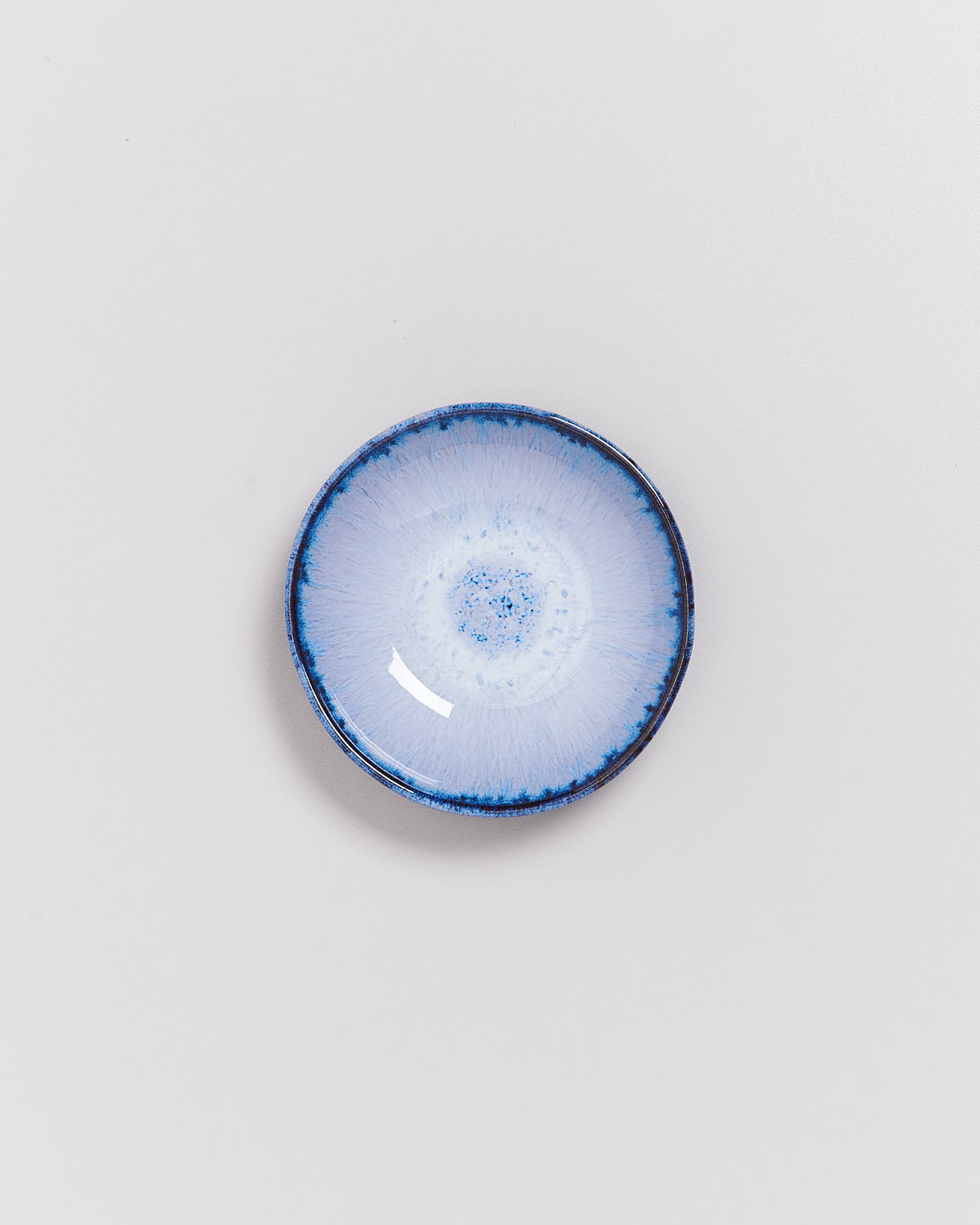 Kleine, runde, blau-weiße Keramikschale mit einem kunstvollen, strahlenförmigen Muster auf der Innenfläche.