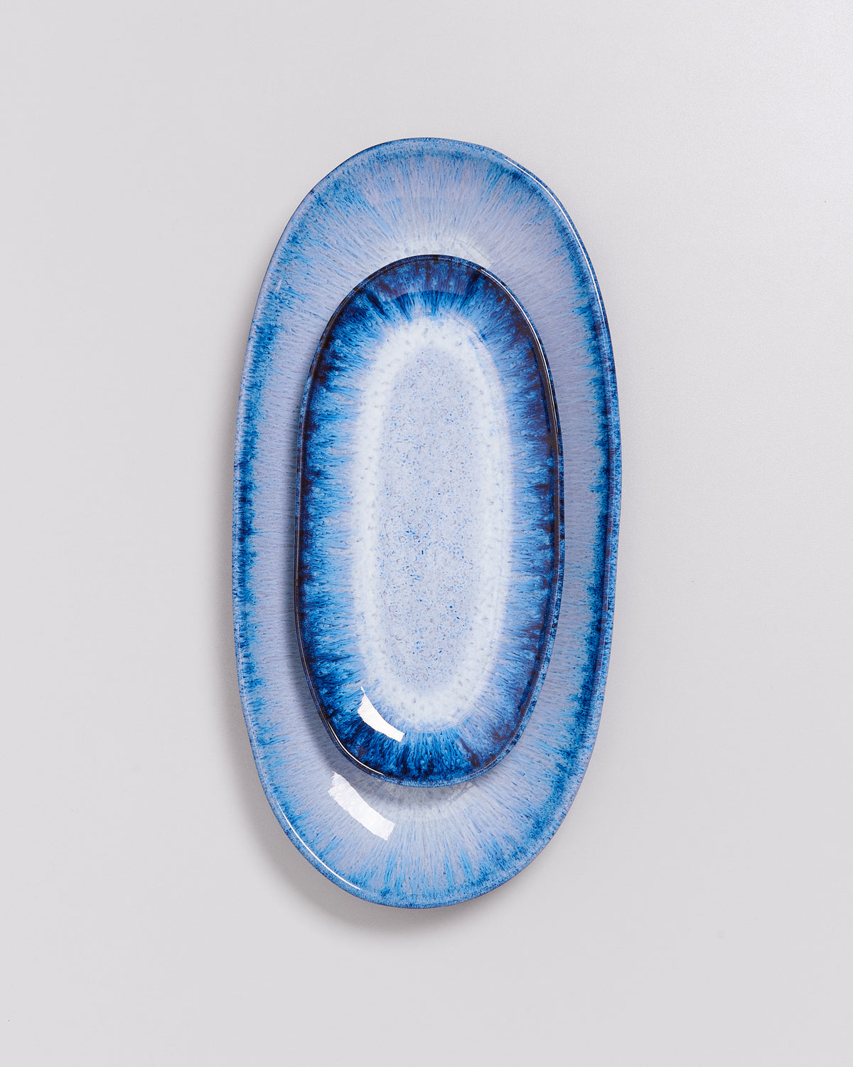 Ovale, blau-weiß gemusterte Keramikplatte mit glänzender Oberfläche auf grauem Hintergrund.