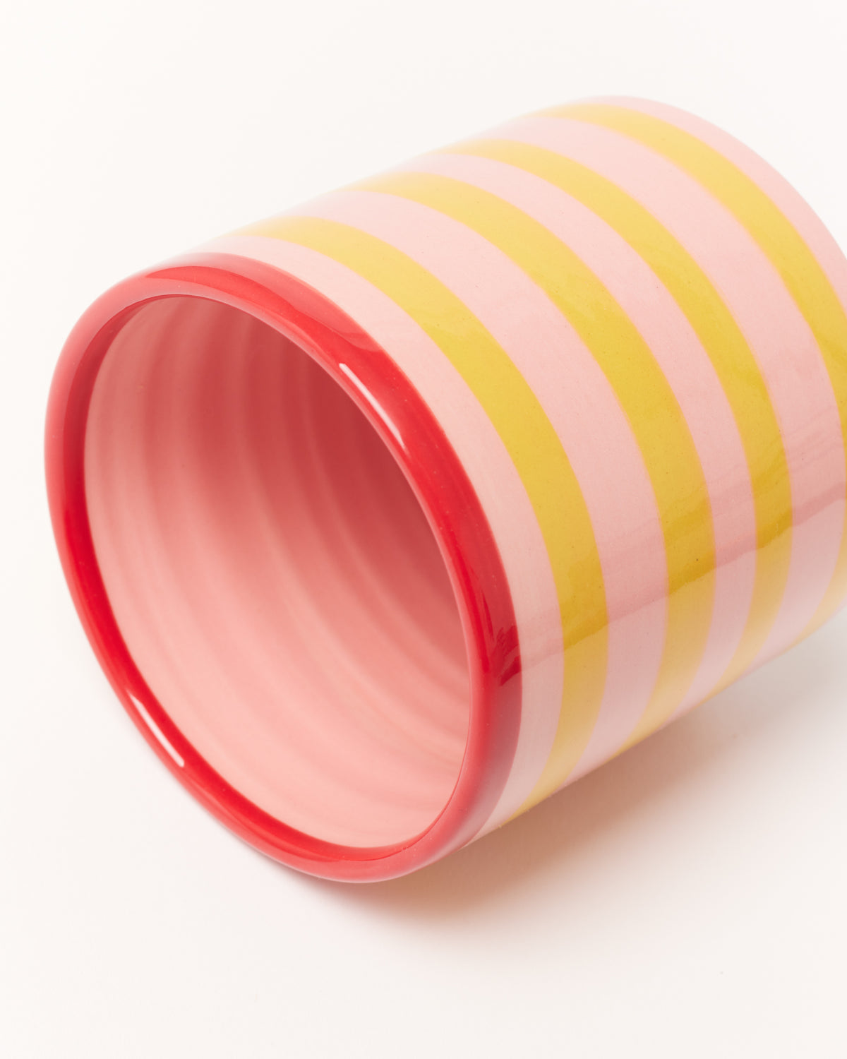 Tasse mit pink-gelben Streifen und rotem Rand, liegend auf weißem Hintergrund.