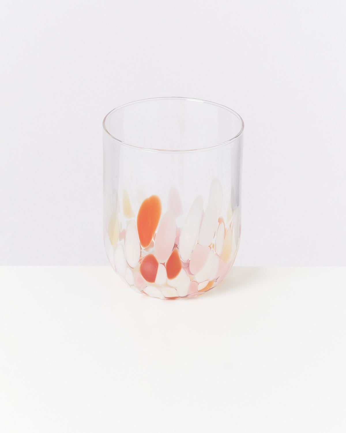 Ein transparentes Glas mit bunten, ovalen Mustern in Rosa und Orange steht auf einer weißen Oberfläche.