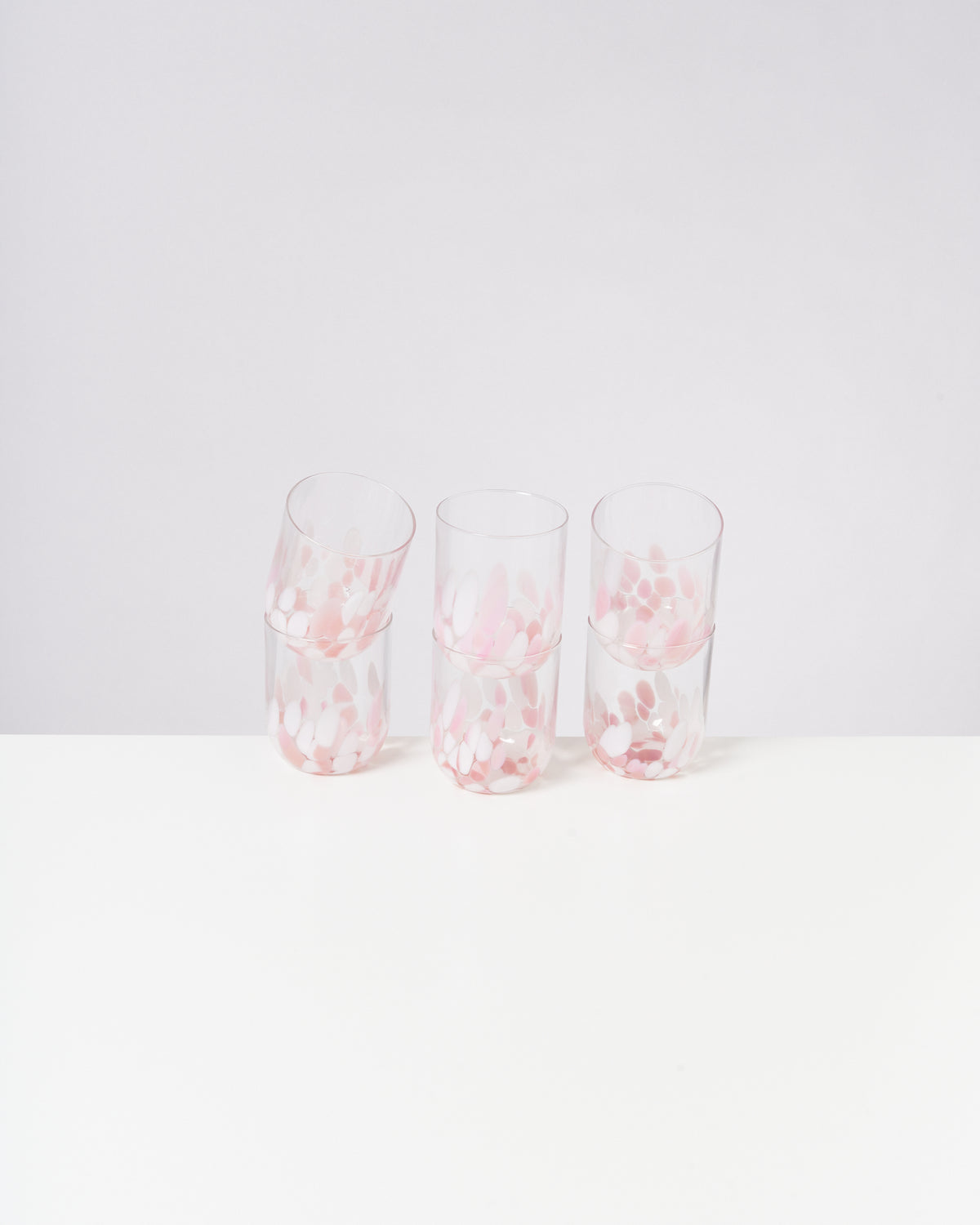 Vier transparente Gläser mit rosa und weißen Mustern stehen auf einem weißen Untergrund.
