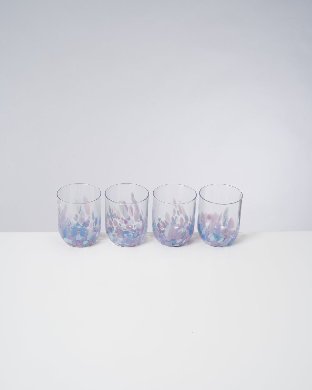 Vier Gläser mit lila und blauen Mustern stehen nebeneinander auf einem weißen Tisch.