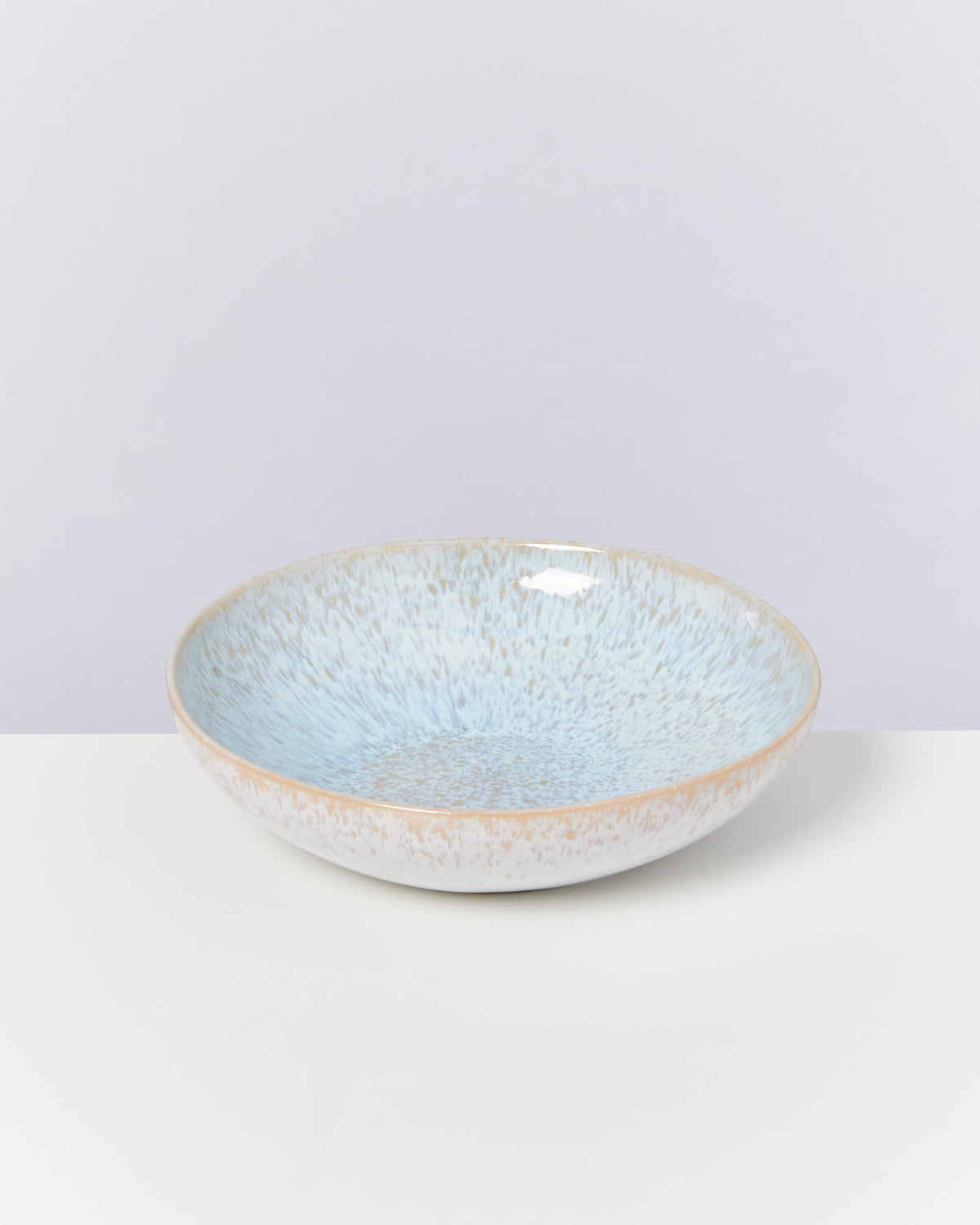Flache, blau-weiße Keramikschale mit gesprenkeltem Muster auf weißem Hintergrund.