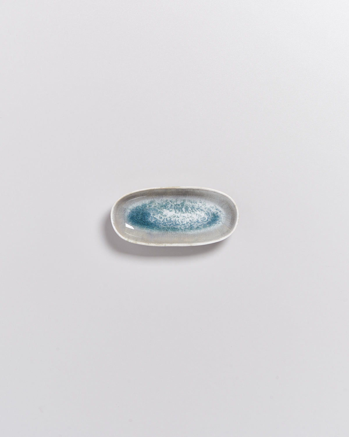 Kleiner, ovaler Teller mit blau-weißer Glasur auf grauem Hintergrund.