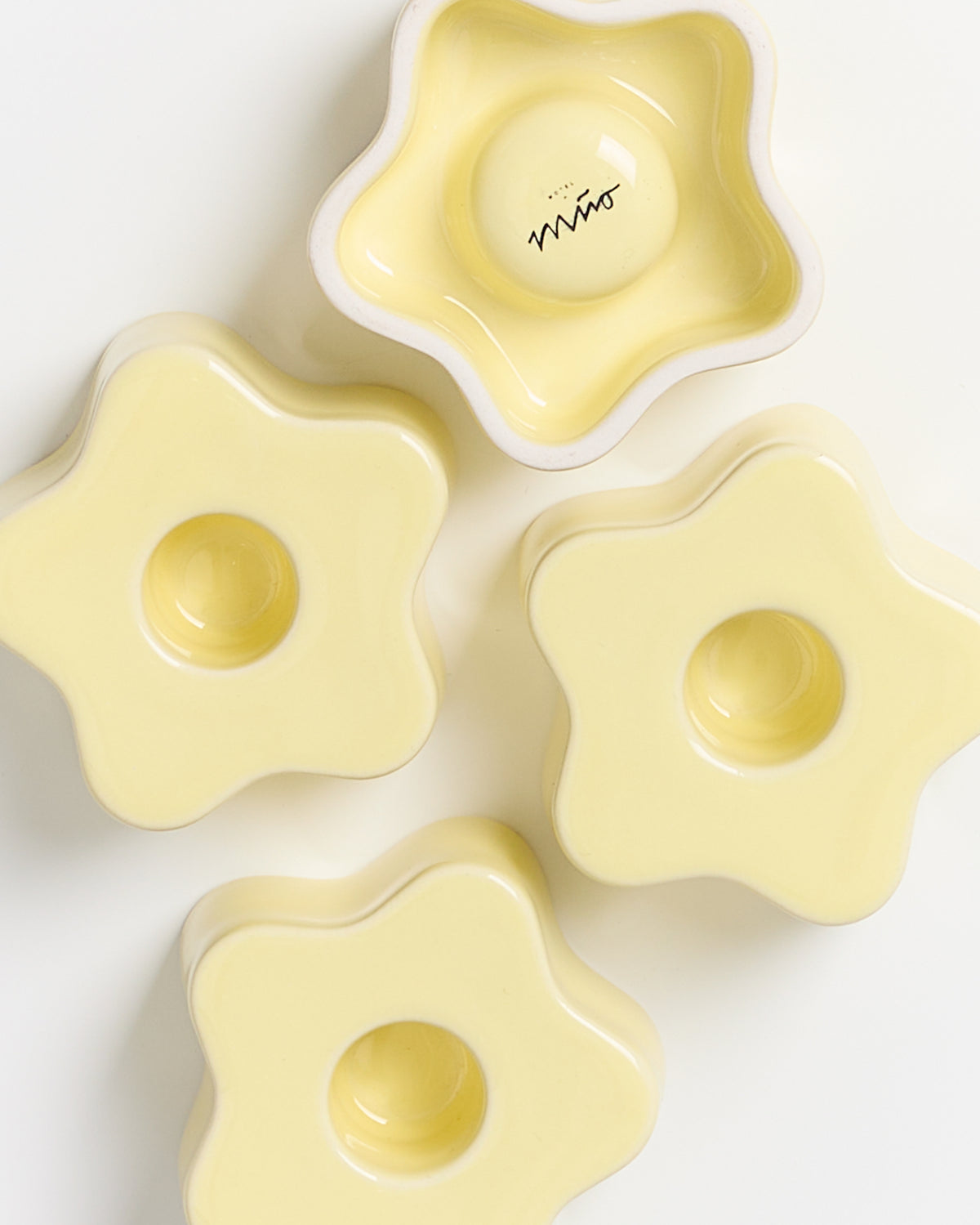 Vier gelbe, blumenförmige Keramikschalen, eine davon mit einem kleinen Schriftzug im Inneren.