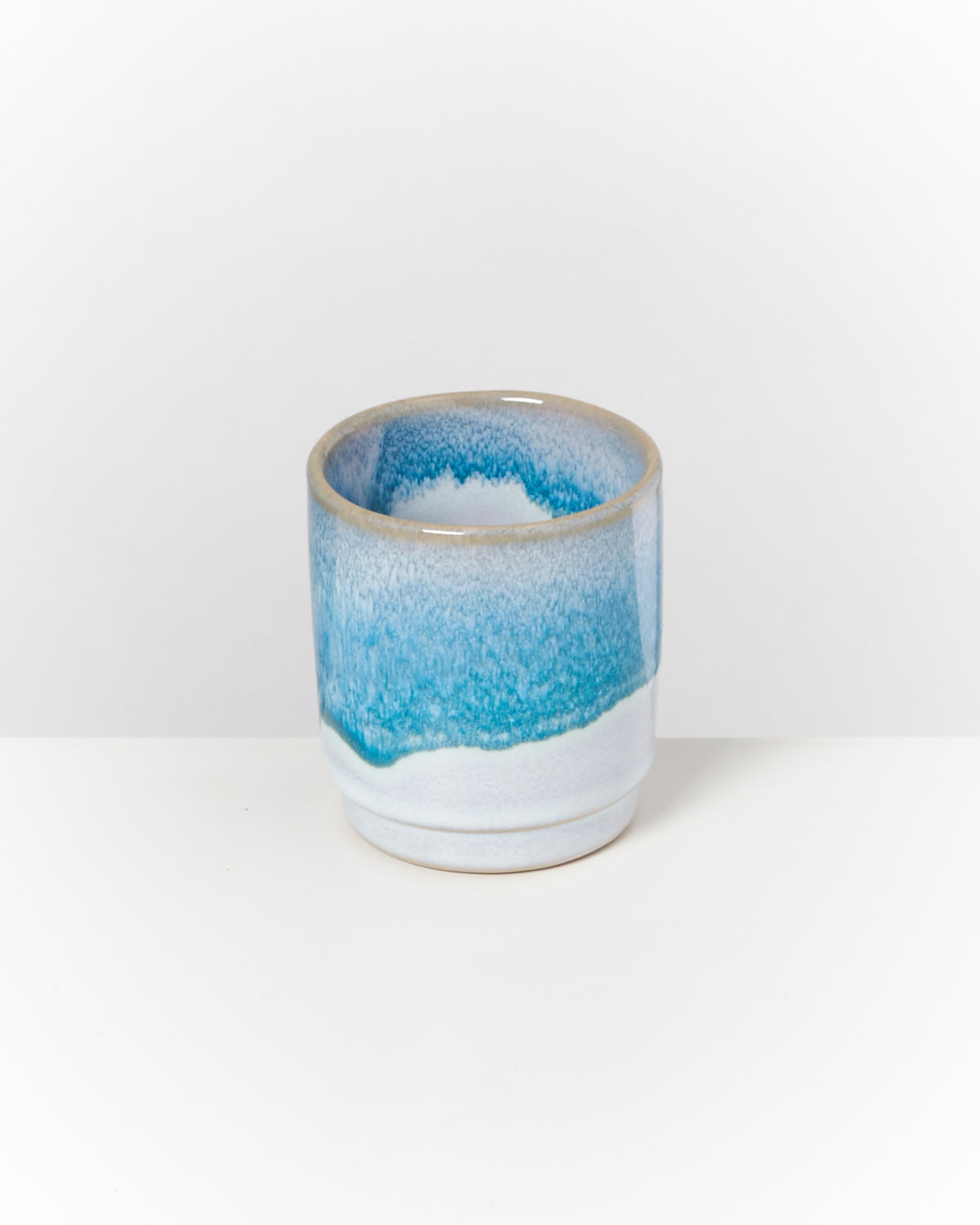 Keramiktasse mit blauer und weißer Glasur auf weißem Hintergrund.