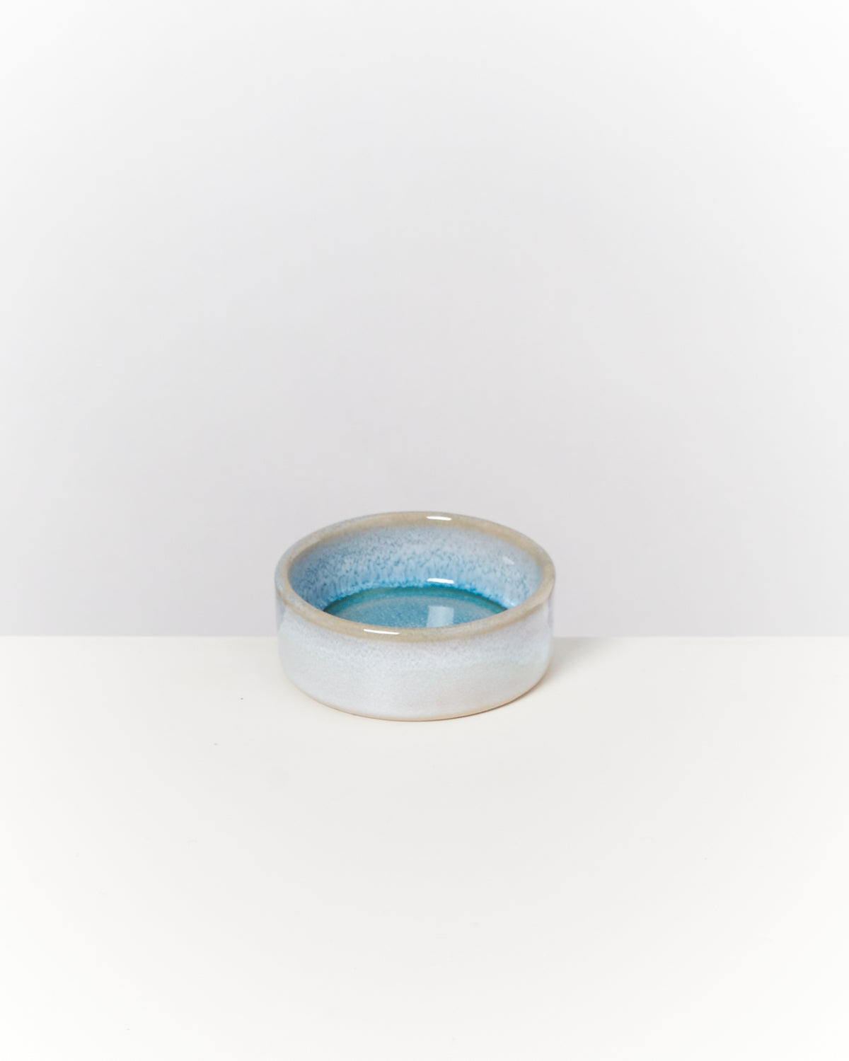 Kleine, runde, blaue Keramikschale mit glänzender Glasur auf weißem Hintergrund.