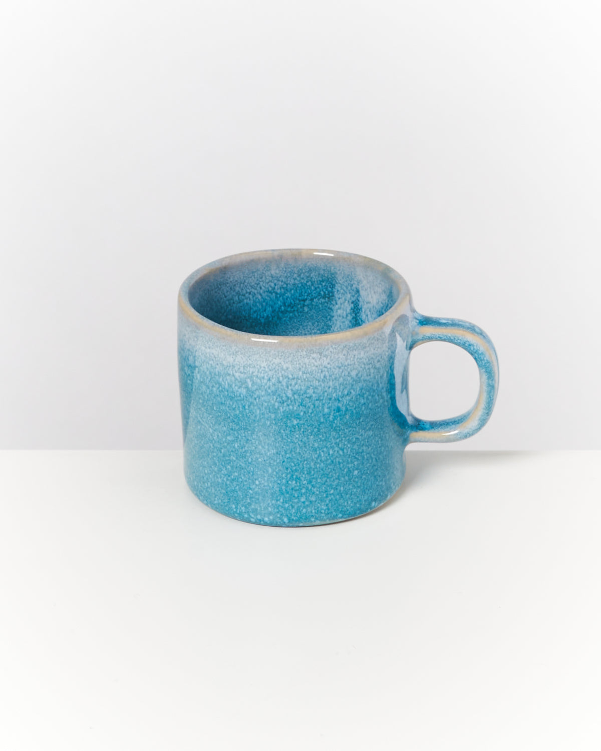 Blaue Keramiktasse mit Henkel steht auf einem weißen Hintergrund.