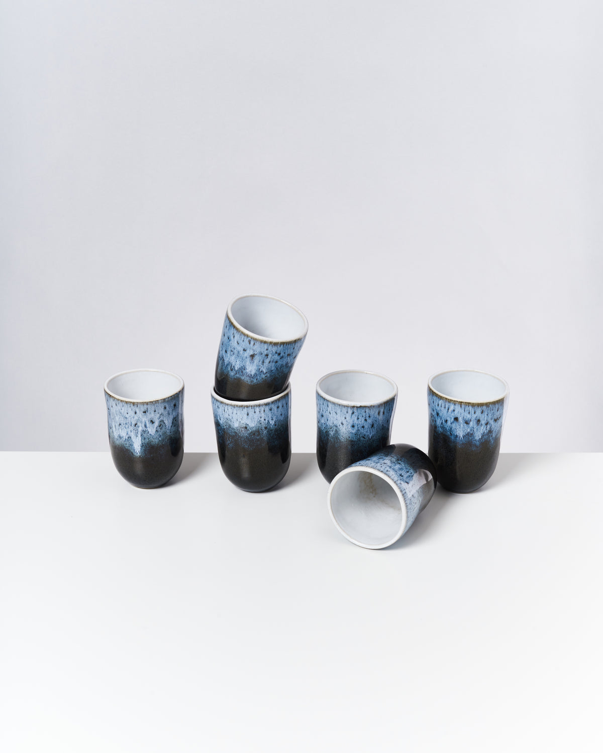 Sechs blau gemusterte Becher in einer unordentlichen Anordnung auf einer weißen Oberfläche.