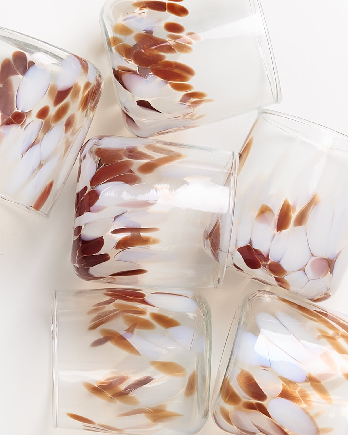 Sechs transparent gefleckte Gläser mit braunen und weißen Mustern liegen auf einer weißen Oberfläche.