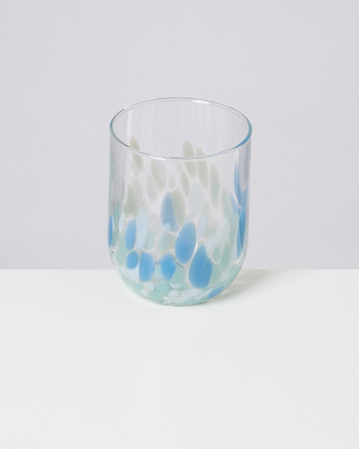 Ein Glas mit blau-weißen Mustern steht auf einem weißen Tisch vor neutralem Hintergrund.