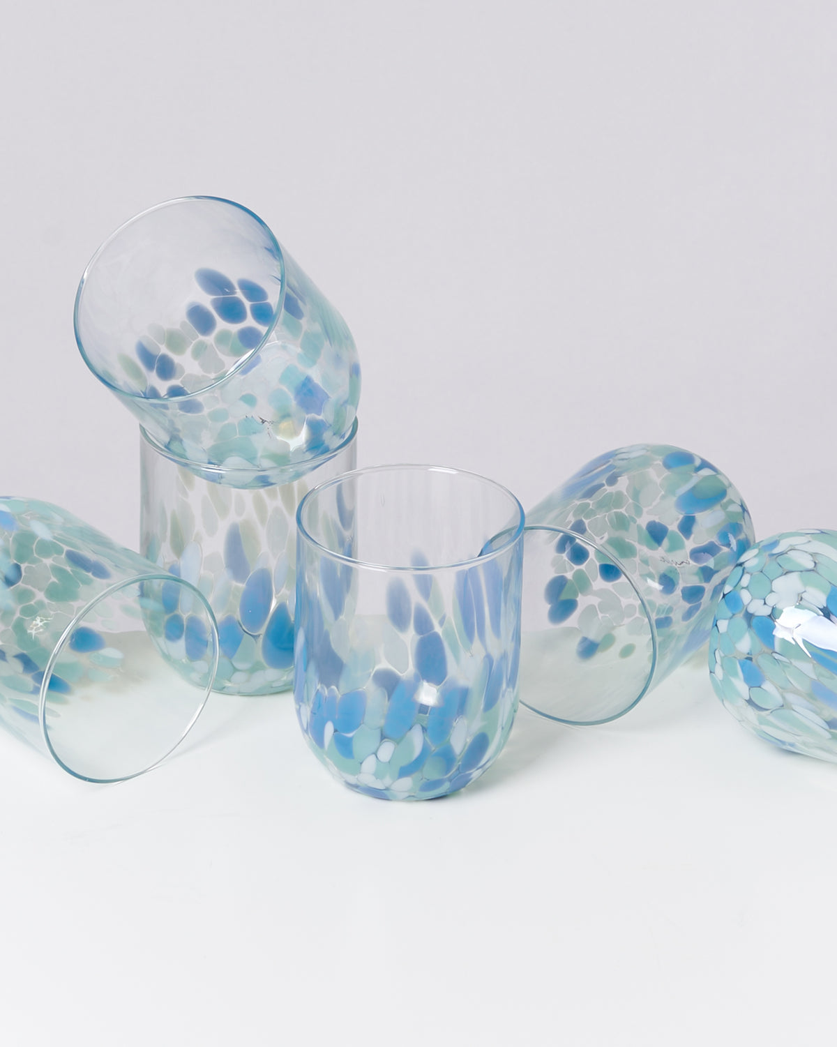 Sechs bunt gepunktete Trinkgläser aus Glas liegen und stehen auf einer weißen Oberfläche.