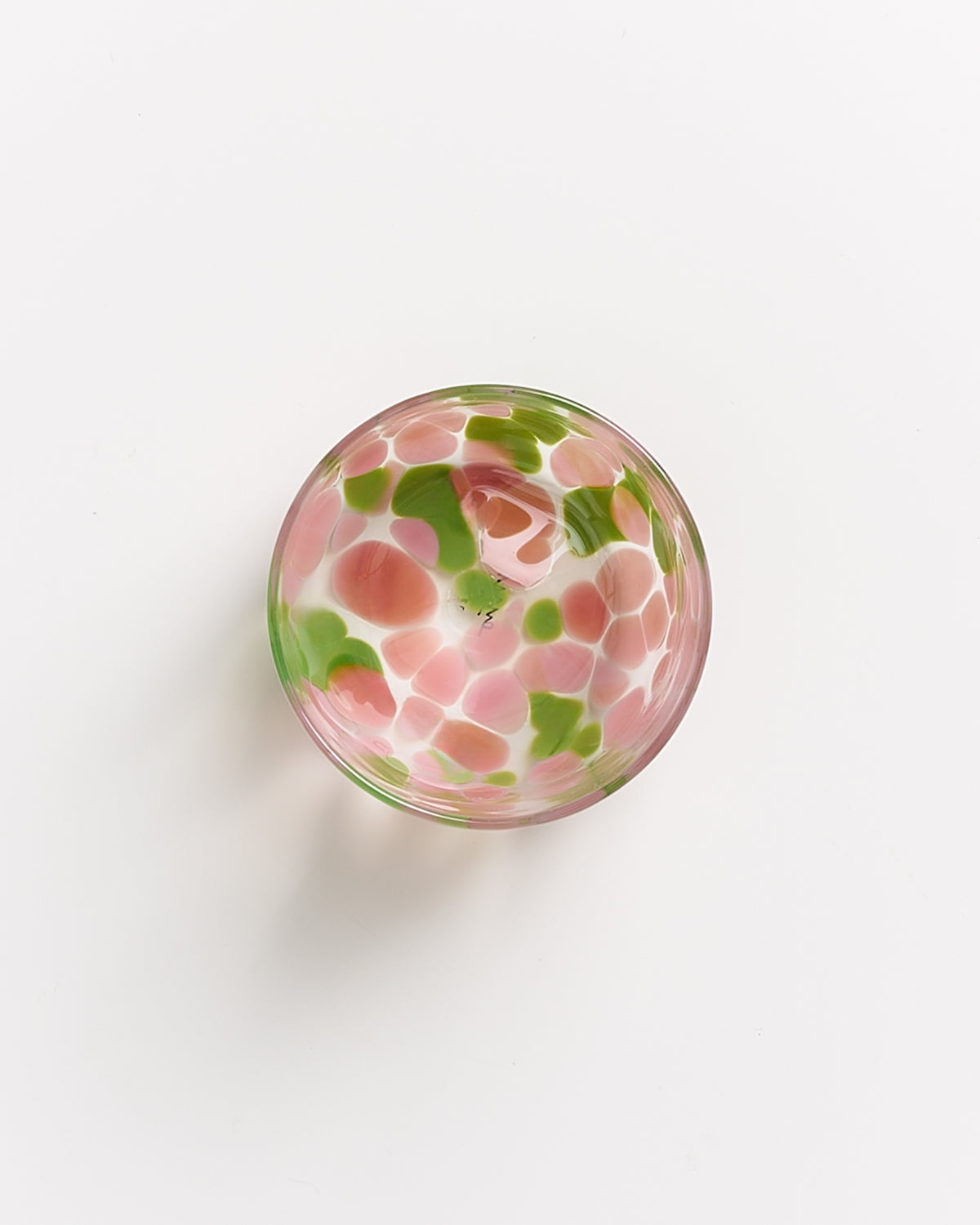 Eine bunte Glasschale mit rosa und grünen Mustern auf weißem Hintergrund.