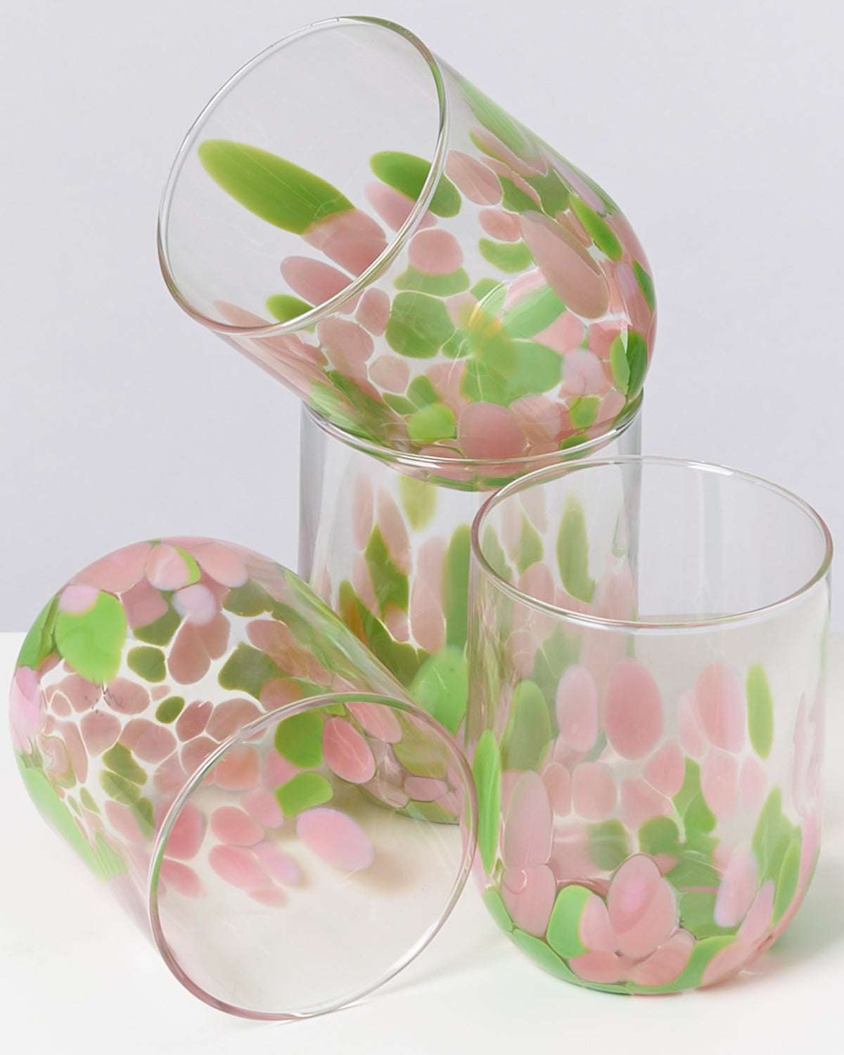 Vier bunte Gläser mit rosa und grünen Tupfen liegen übereinander auf einem weißen Hintergrund.