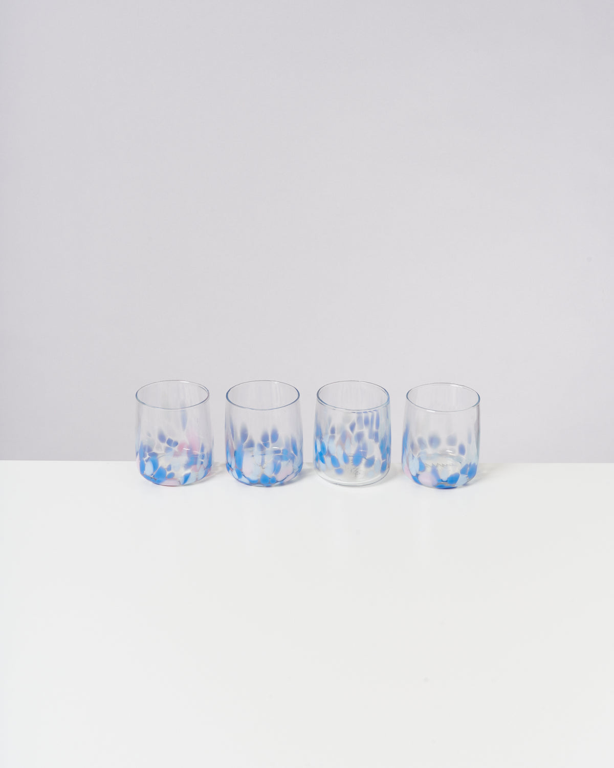 Vier Gläser mit blauem Tupfenmuster stehen in einer Reihe auf einem weißen Tisch.