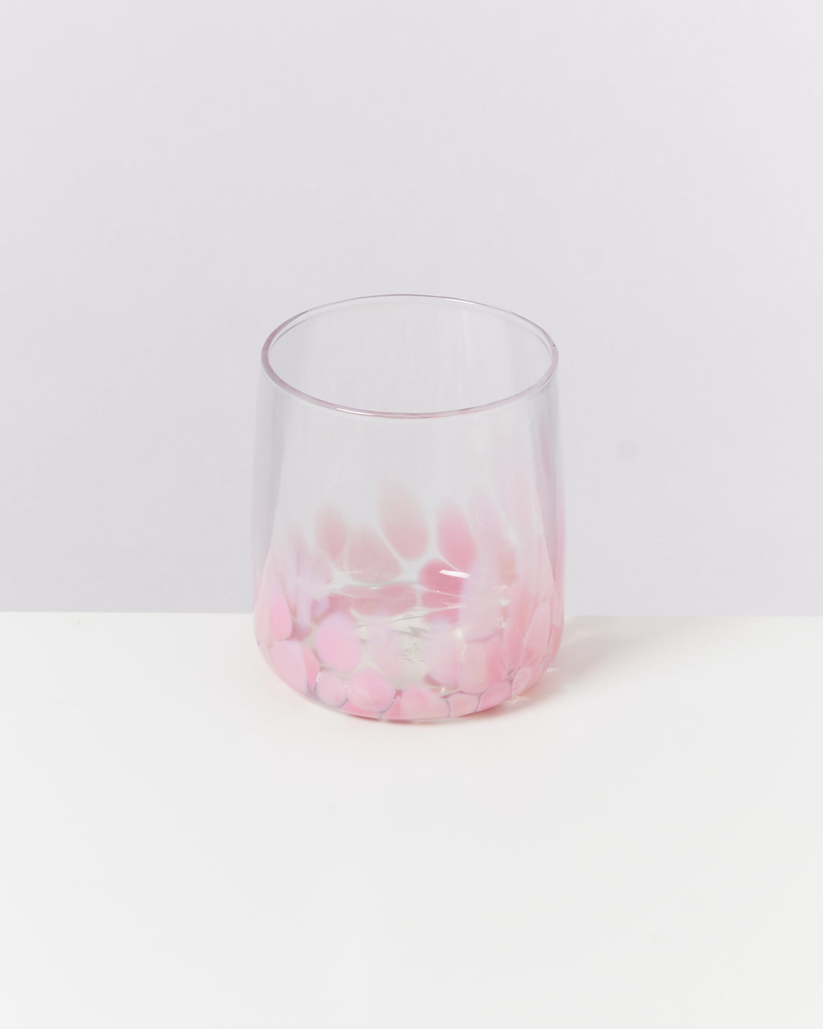 Ein Glas mit rosa und weißen Mustern steht auf einer weißen Oberfläche vor einem hellgrauen Hintergrund.