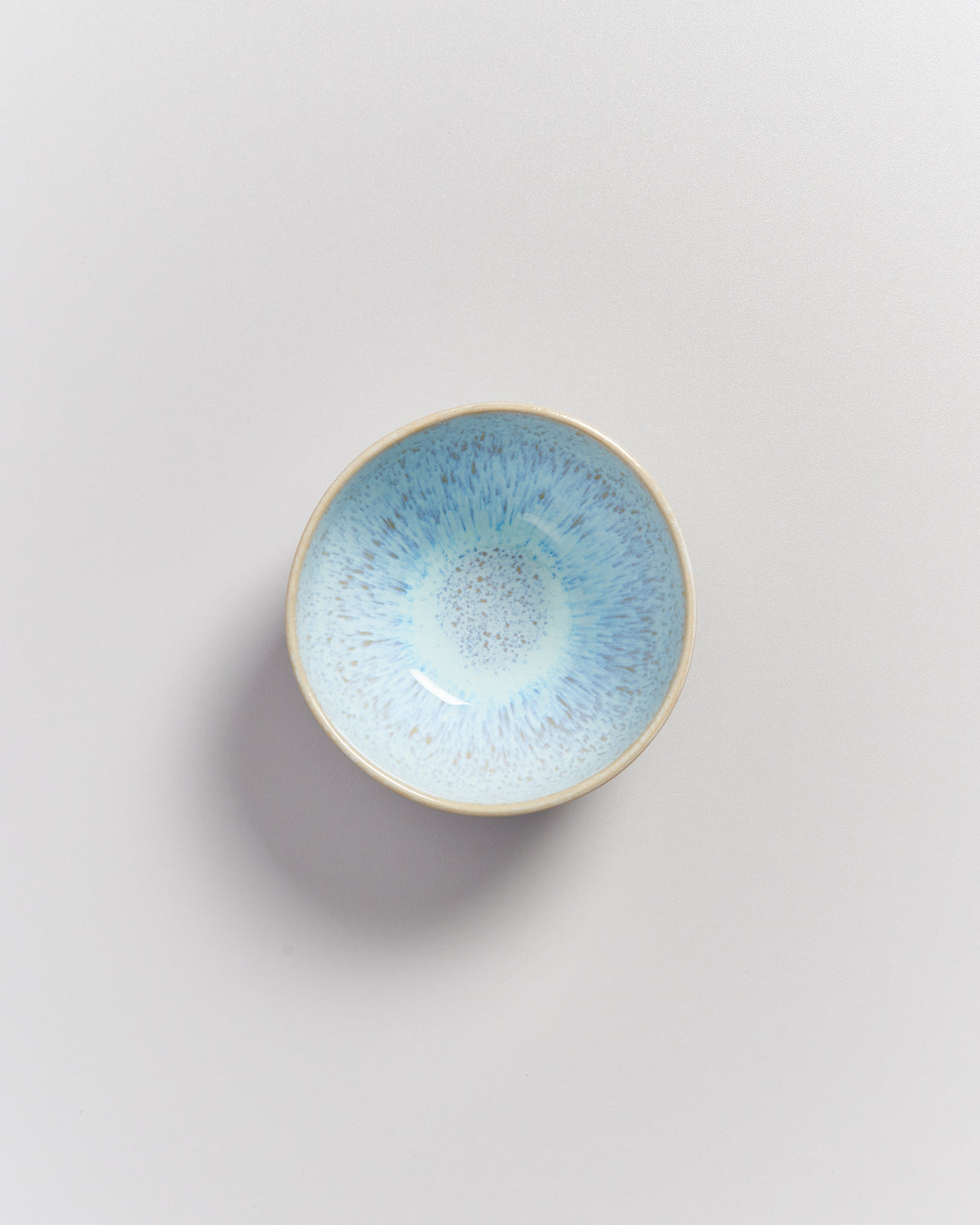Kleine Schale mit blauem, gesprenkeltem Innendesign auf einer hellen, glatten Oberfläche.