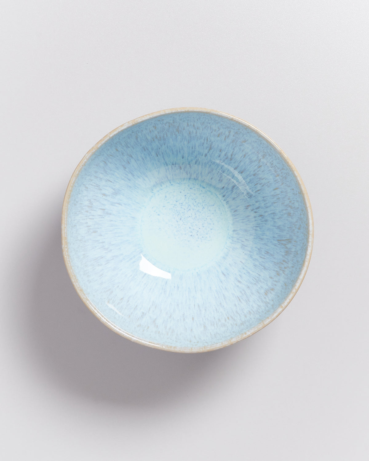 Blaue Keramikschale mit glasiertem, gesprenkeltem Inneren und rauem Rand auf hellem Hintergrund.