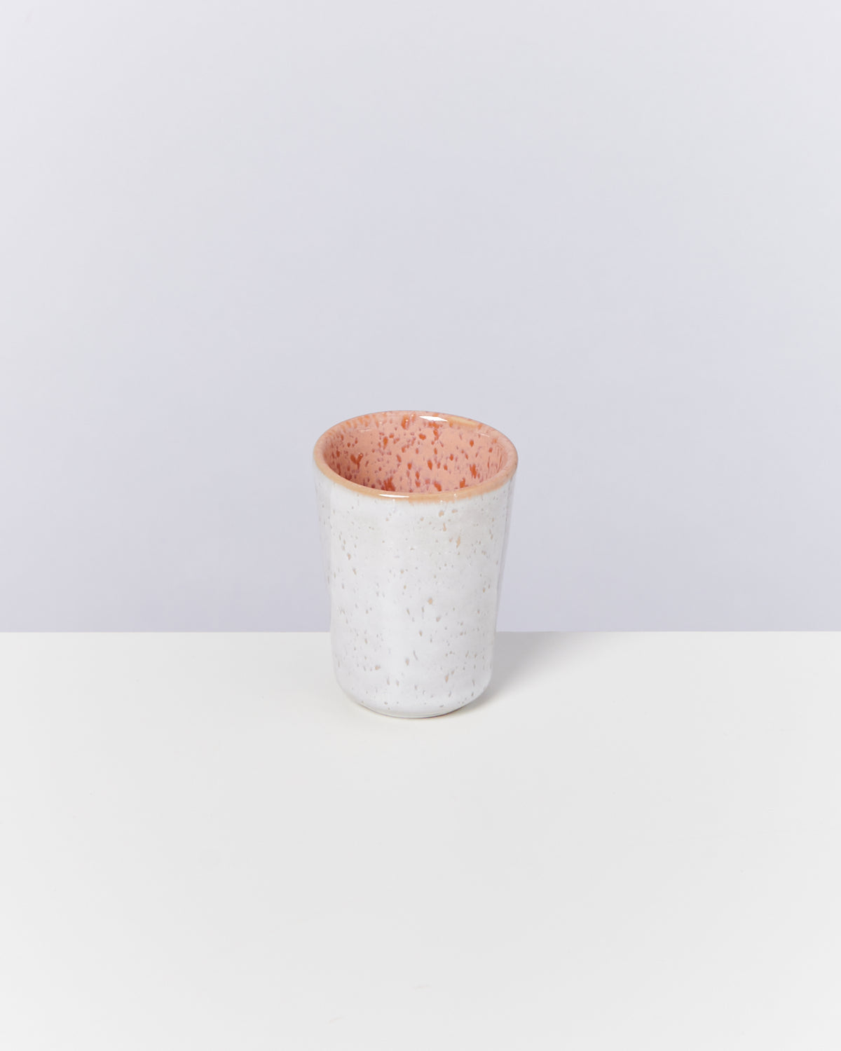 Keramikbecher mit weißer Außenseite und rosa gesprenkeltem Inneren auf weißem Untergrund.