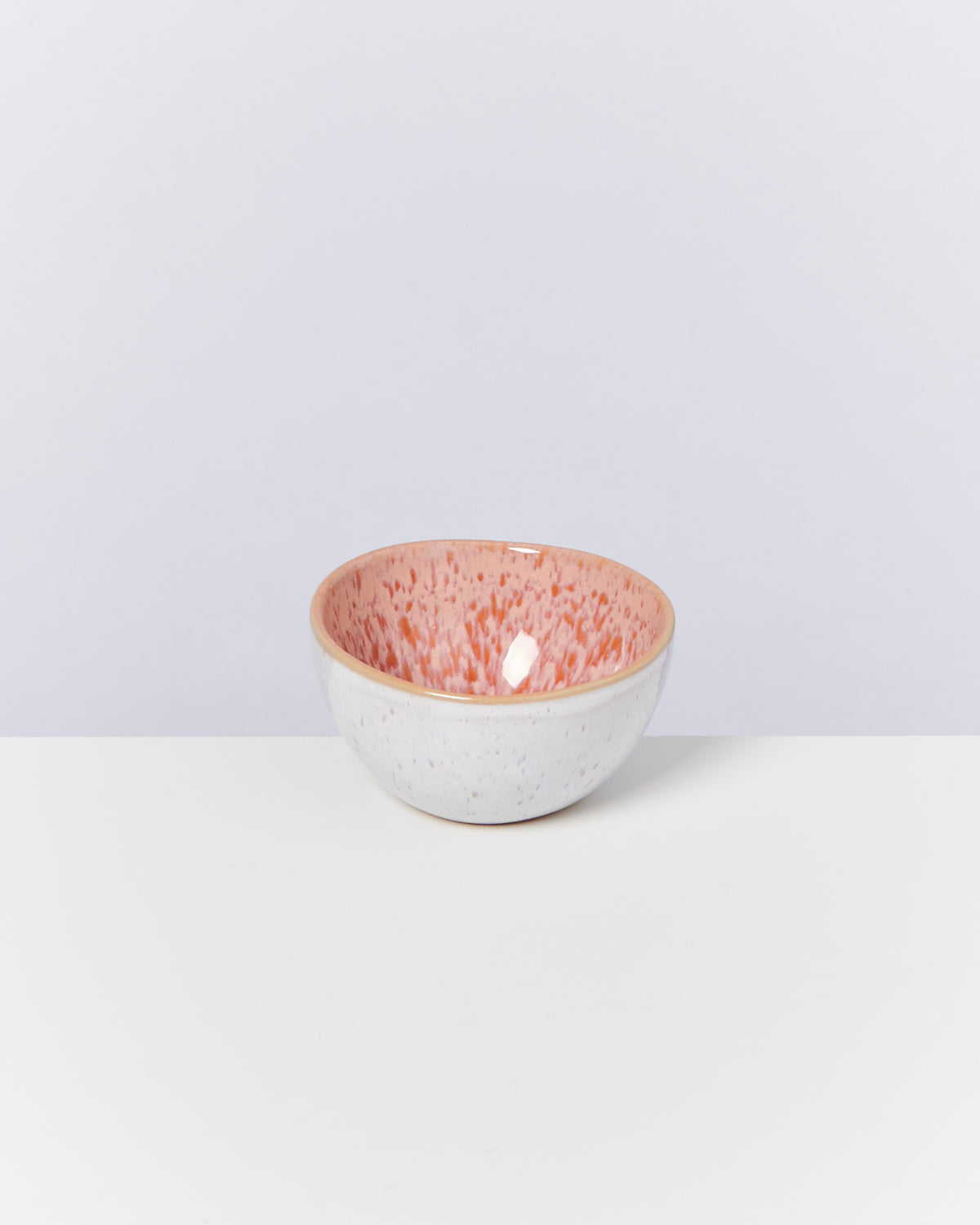 Keramikschale mit weißer Außenseite und rosa Sprenkeln auf der Innenseite, auf einer weißen Fläche platziert.