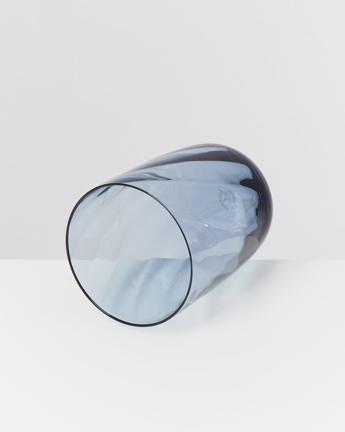 Blaues, transparentes Glas mit zylindrischer Form liegt auf weißem Hintergrund.